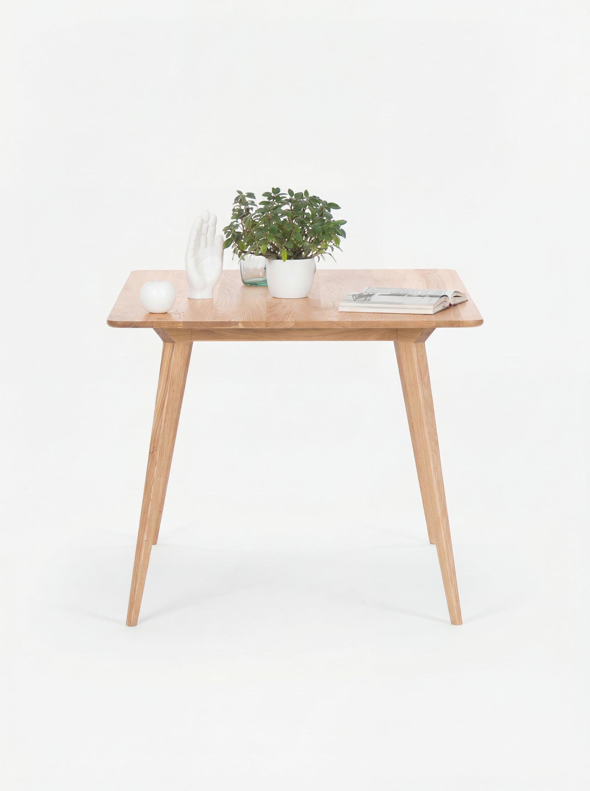 Wooden table with a plant, decorative white hand, a candle, and a magazine on top.