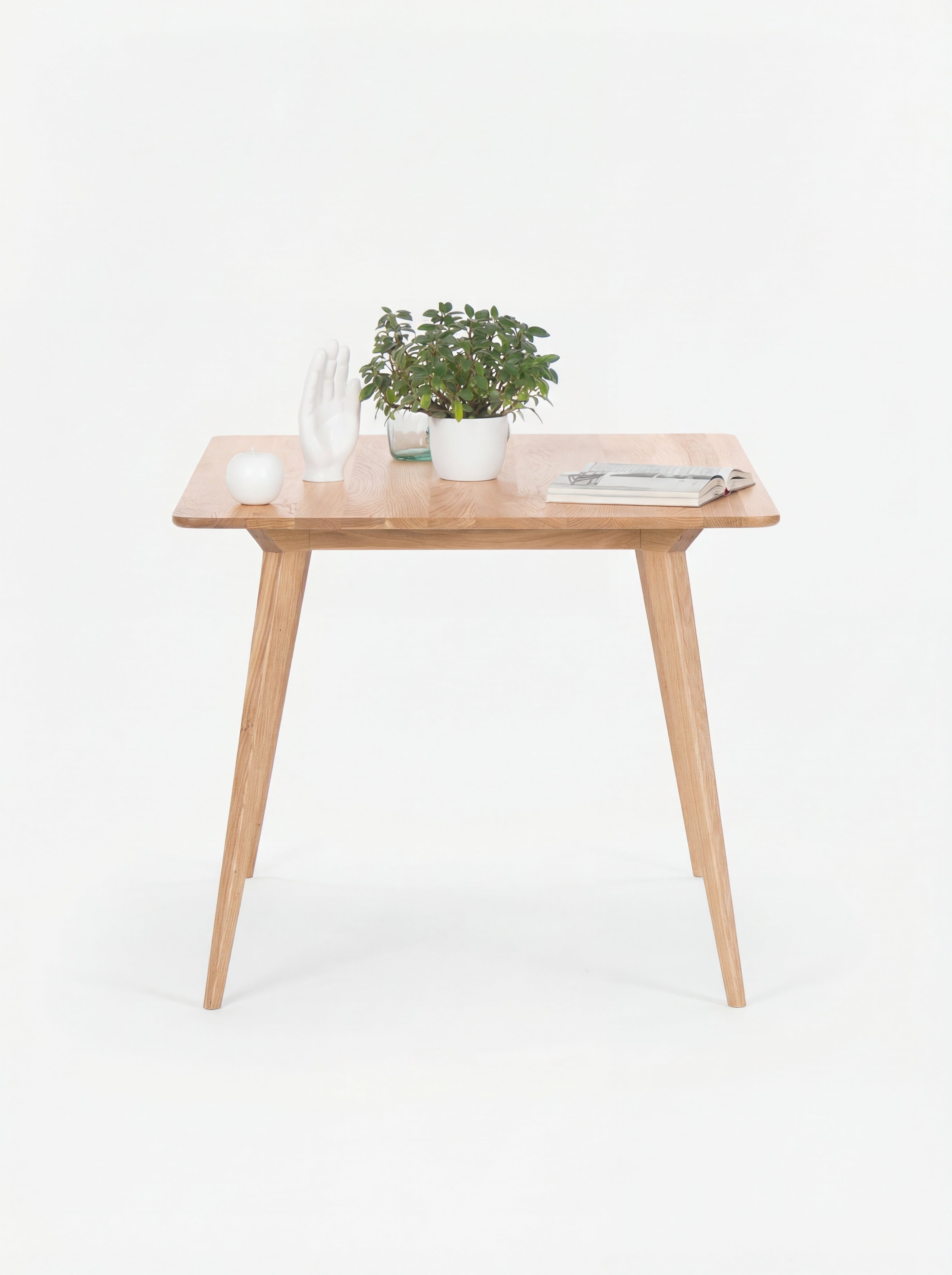 Wooden table with a plant, decorative white hand, a candle, and a magazine on top.