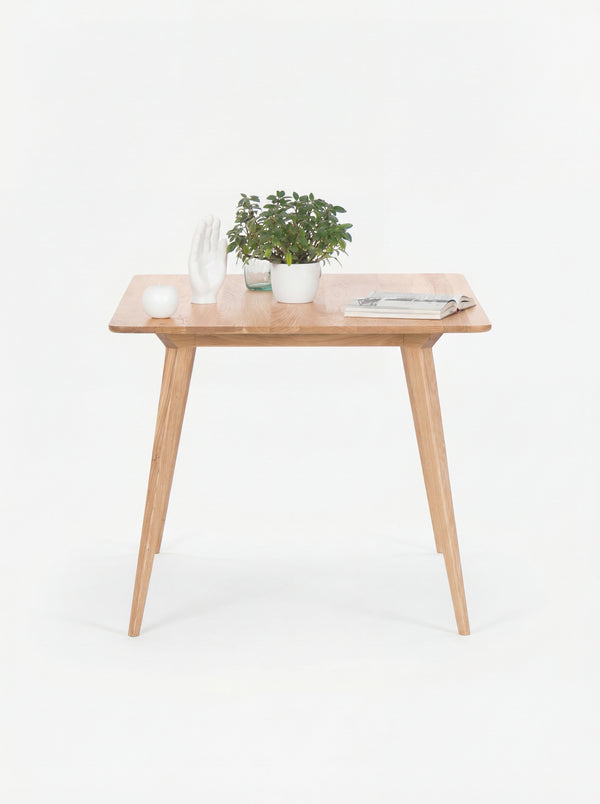 Wooden table with a plant, decorative white hand, a candle, and a magazine on top.