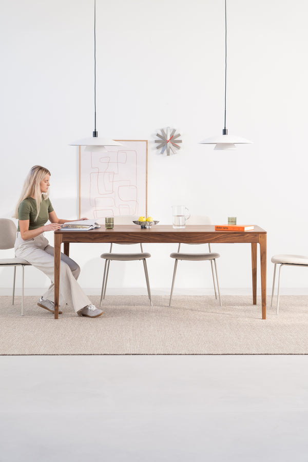Woman sitting at a wooden table with a book, minimalist decor, pendant lights overhead.