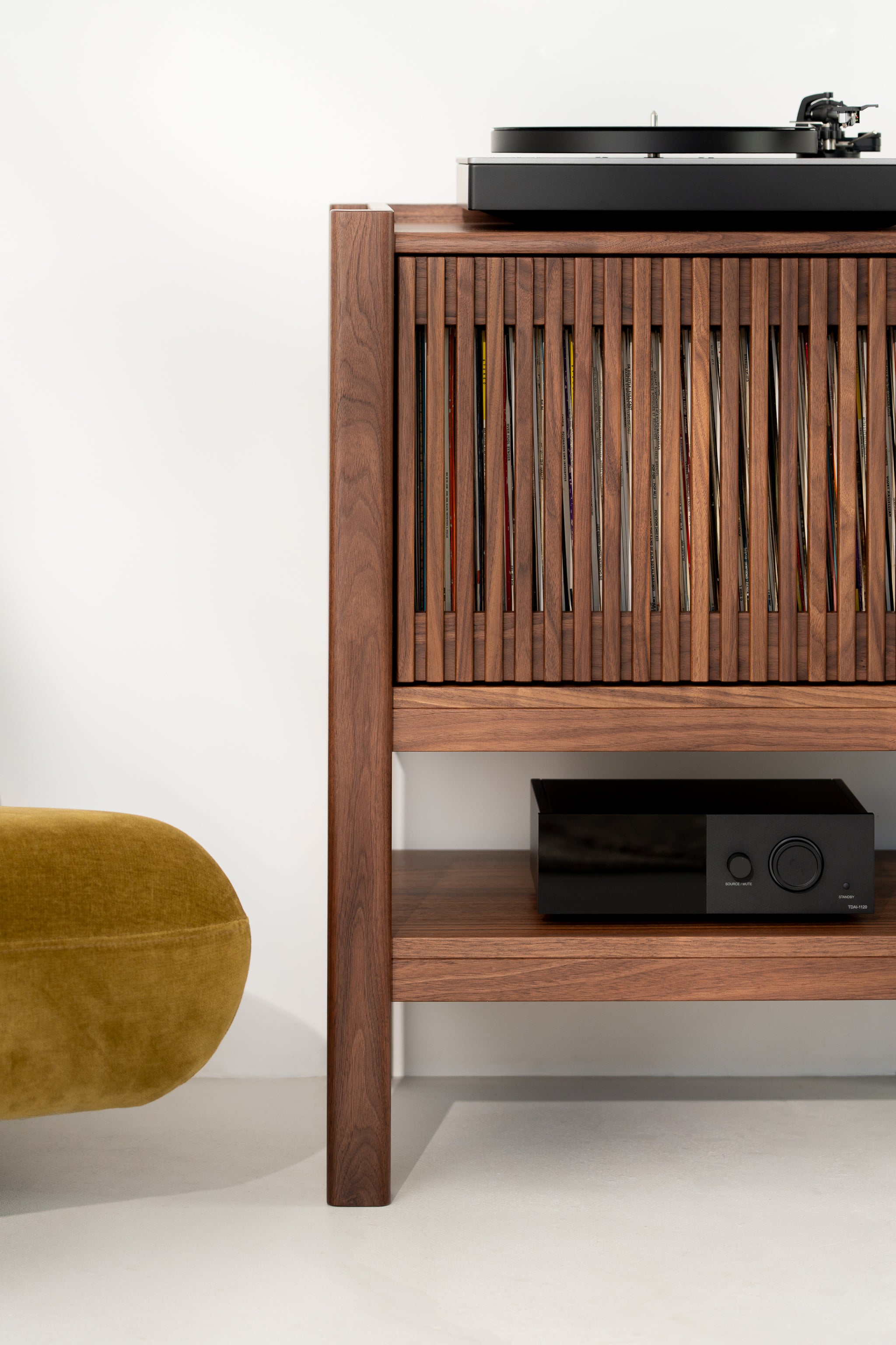 Wooden record cabinet with a turntable on top and audio equipment below. A yellow pouf is partially visible.
