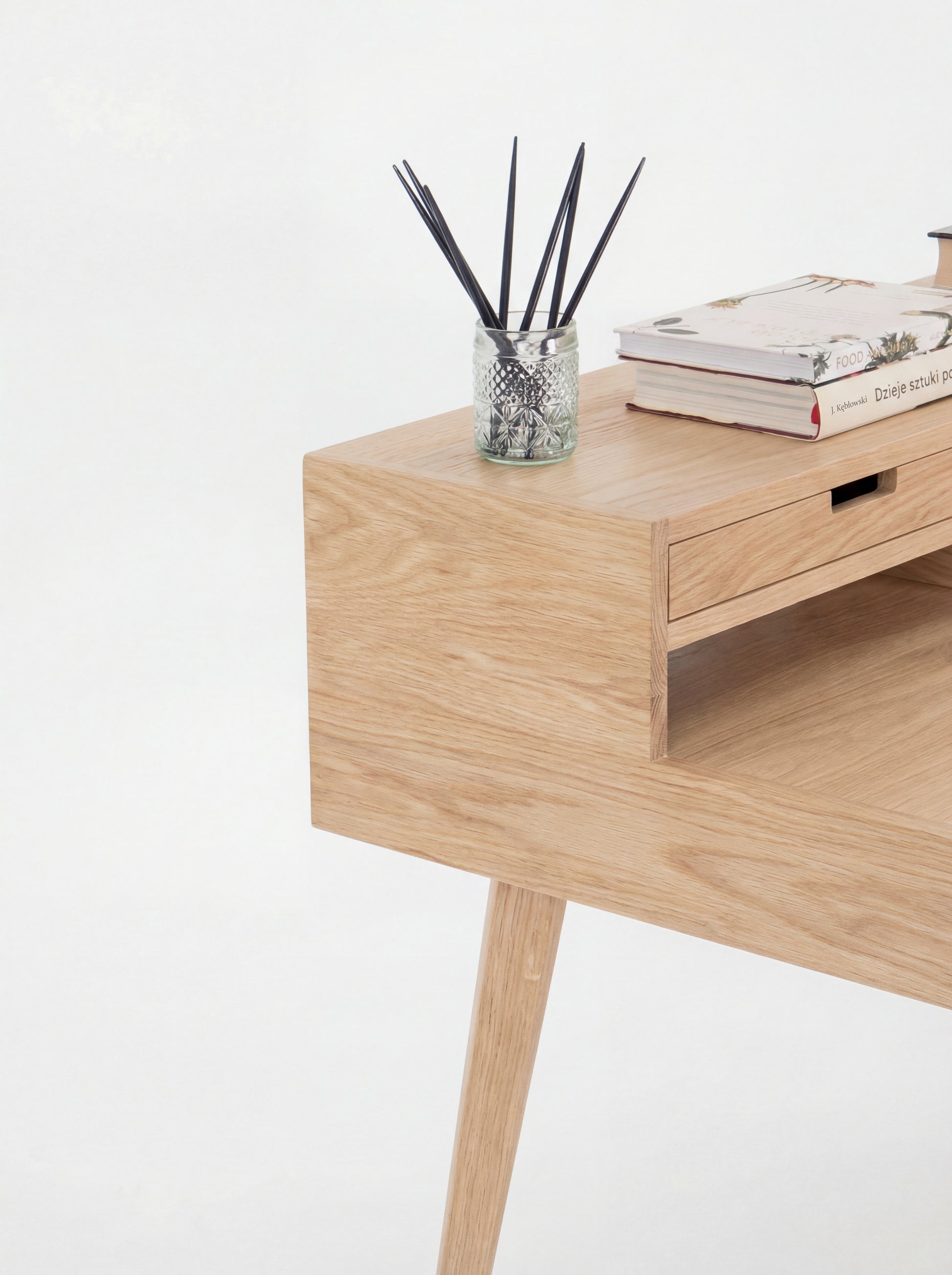 Wooden desk with a jar of black sticks and books on top.