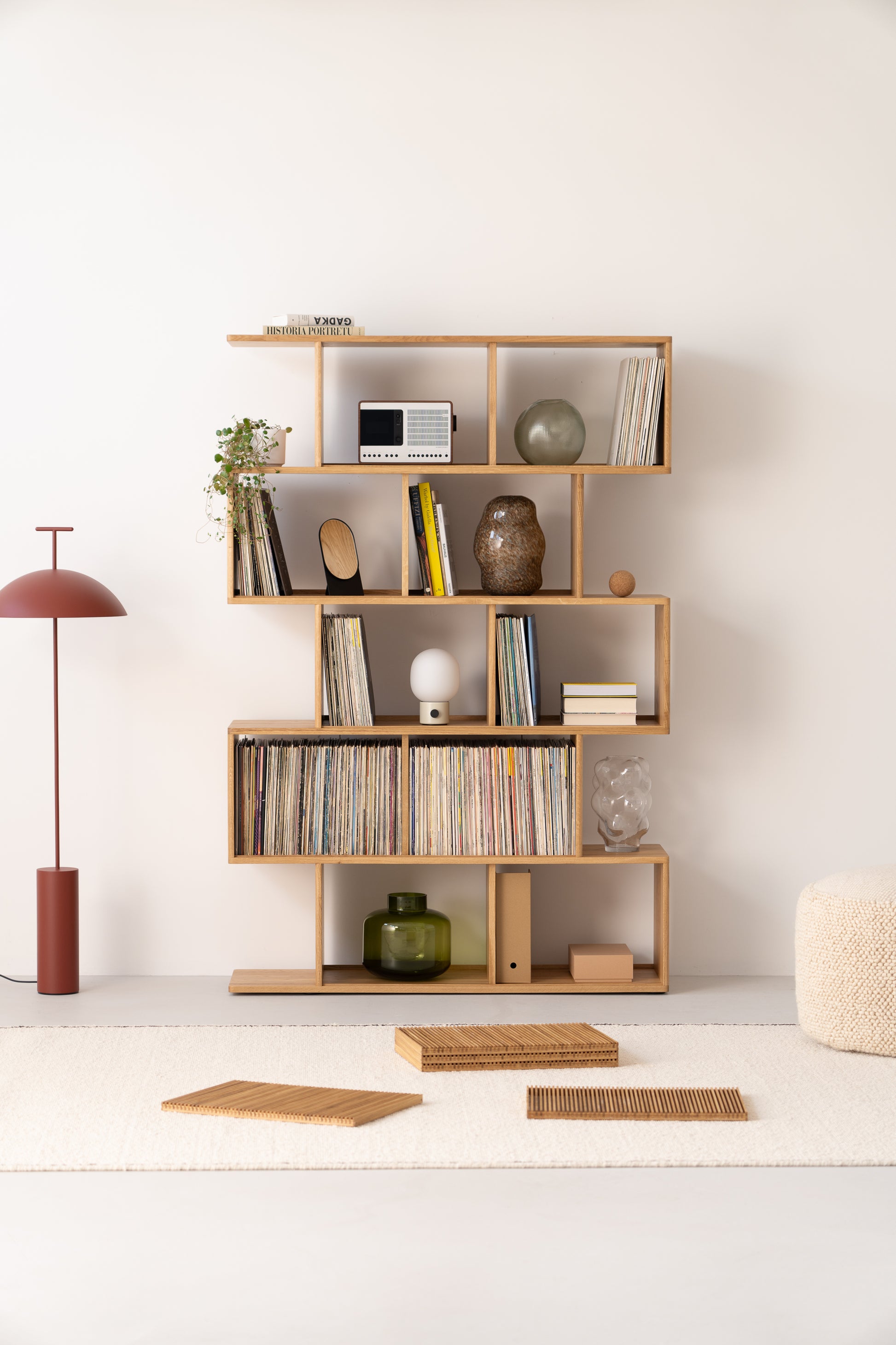 Wooden shelving with books, records, and decor next to a red floor lamp on a light rug.