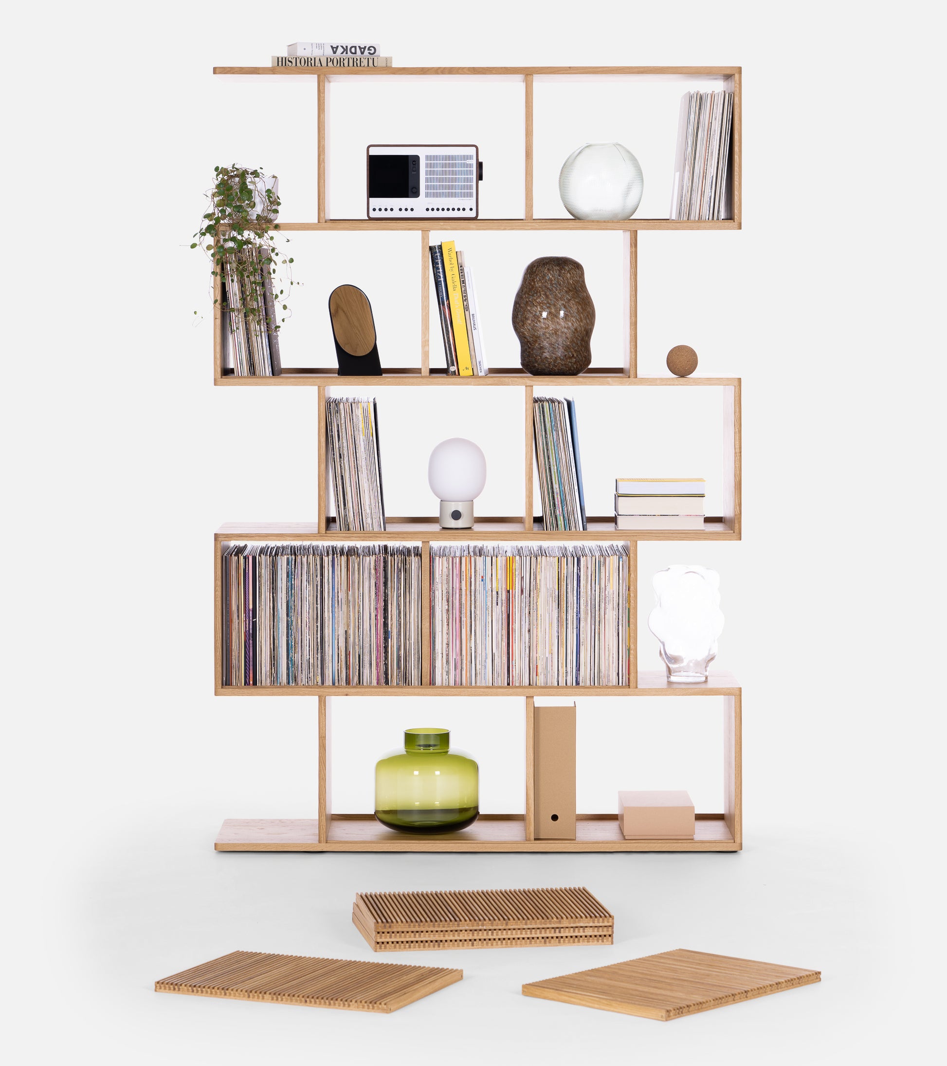 Wooden shelf displaying books, records, décor items, and a plant with two wooden grids on the floor.