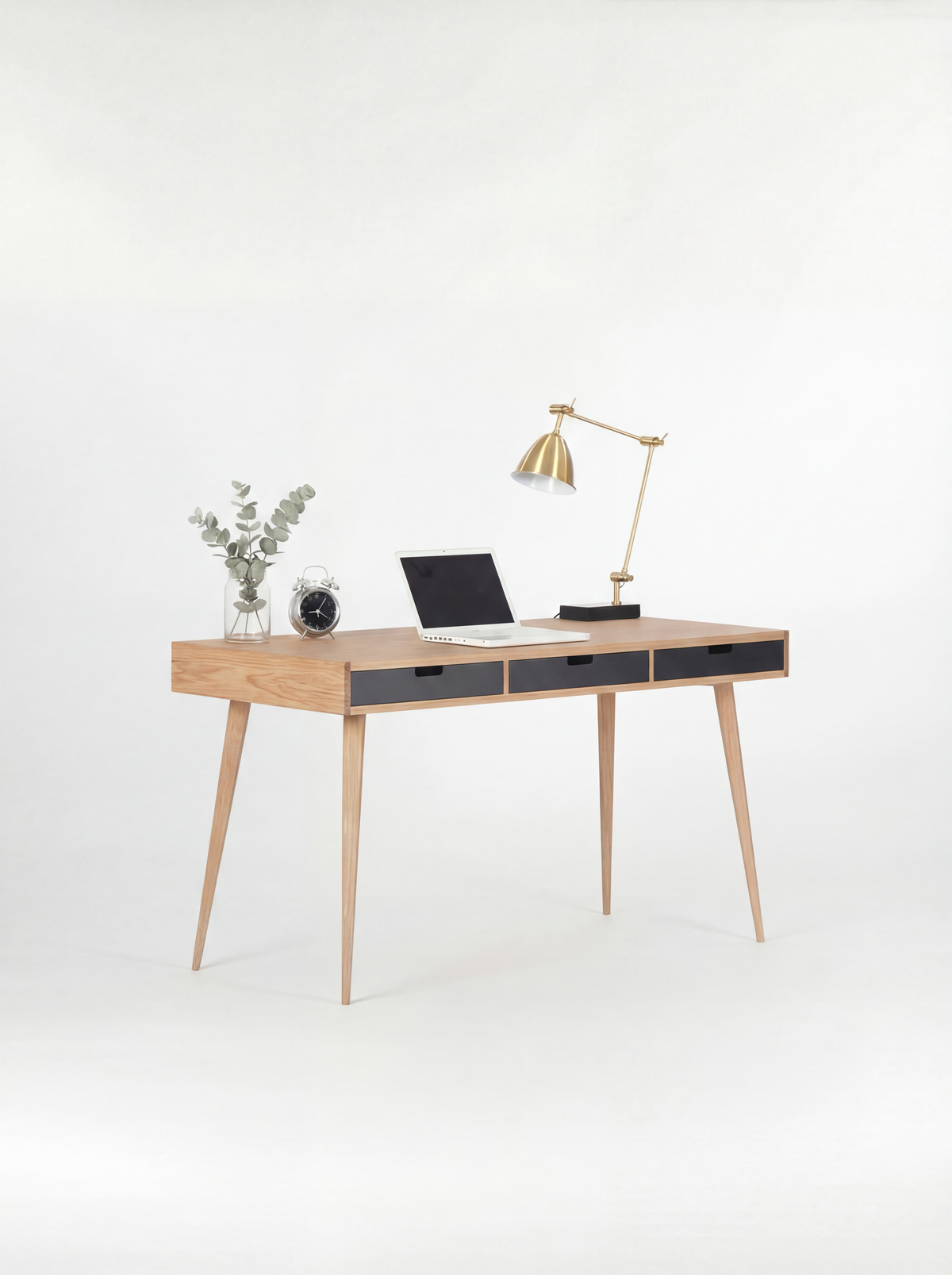 HEIM 140 desk in oak wood at an angle, with three black drawer fronts, a brass lamp and laptop