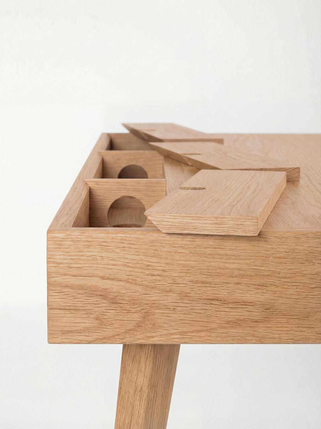 Back corner of the HEIM 140 desk in oak wood, with raised cable flaps exposing compartments and round holes