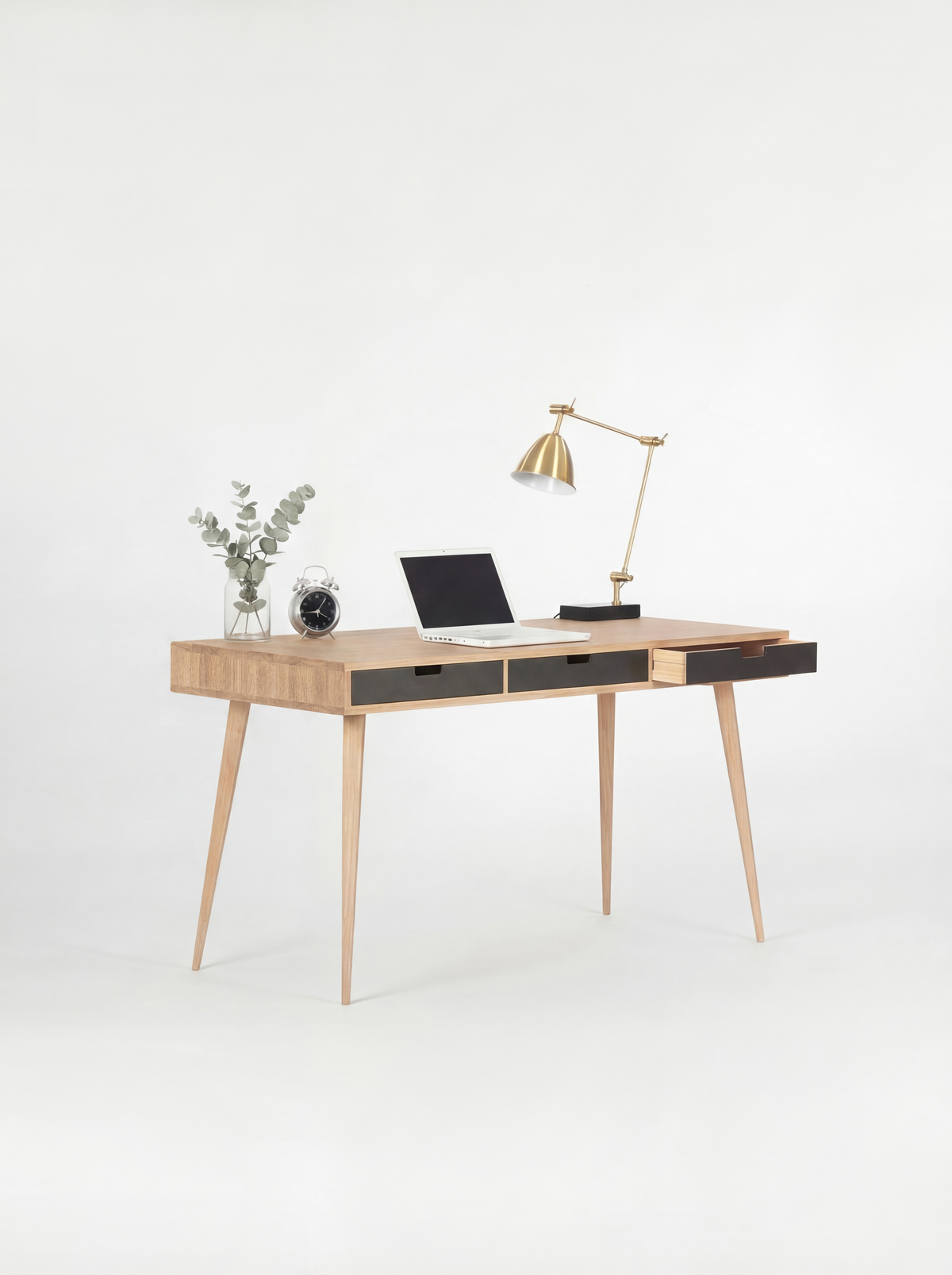 Angled view of the HEIM 140 desk in solid oak, with three black drawer fronts and the right drawer pulled out