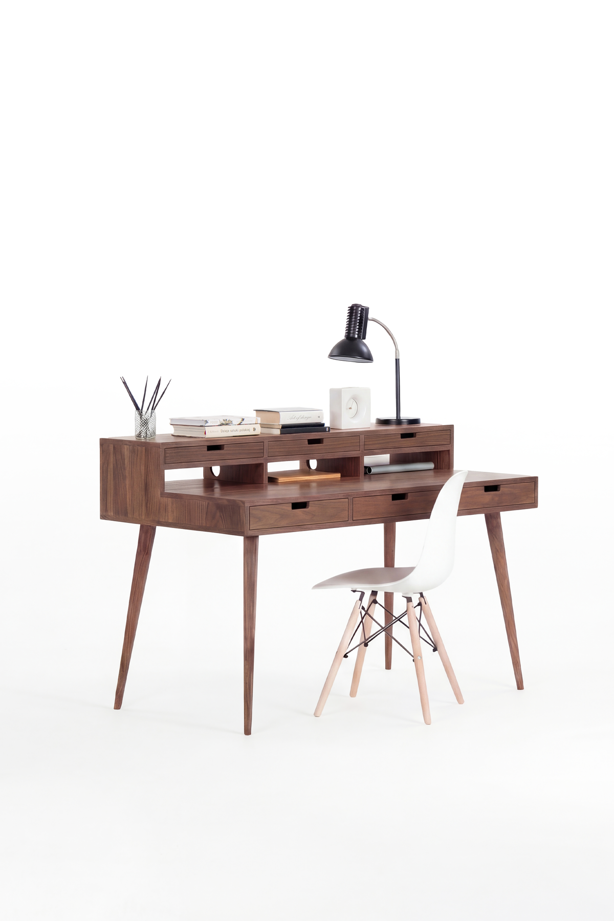 HEIM 140 desk in solid walnut, three-quarter view with a lamp, books and a clock on the hutch