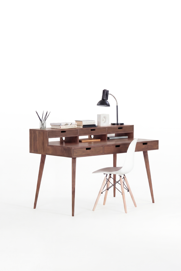 HEIM 140 desk in solid walnut, three-quarter view with a lamp, books and a clock on the hutch