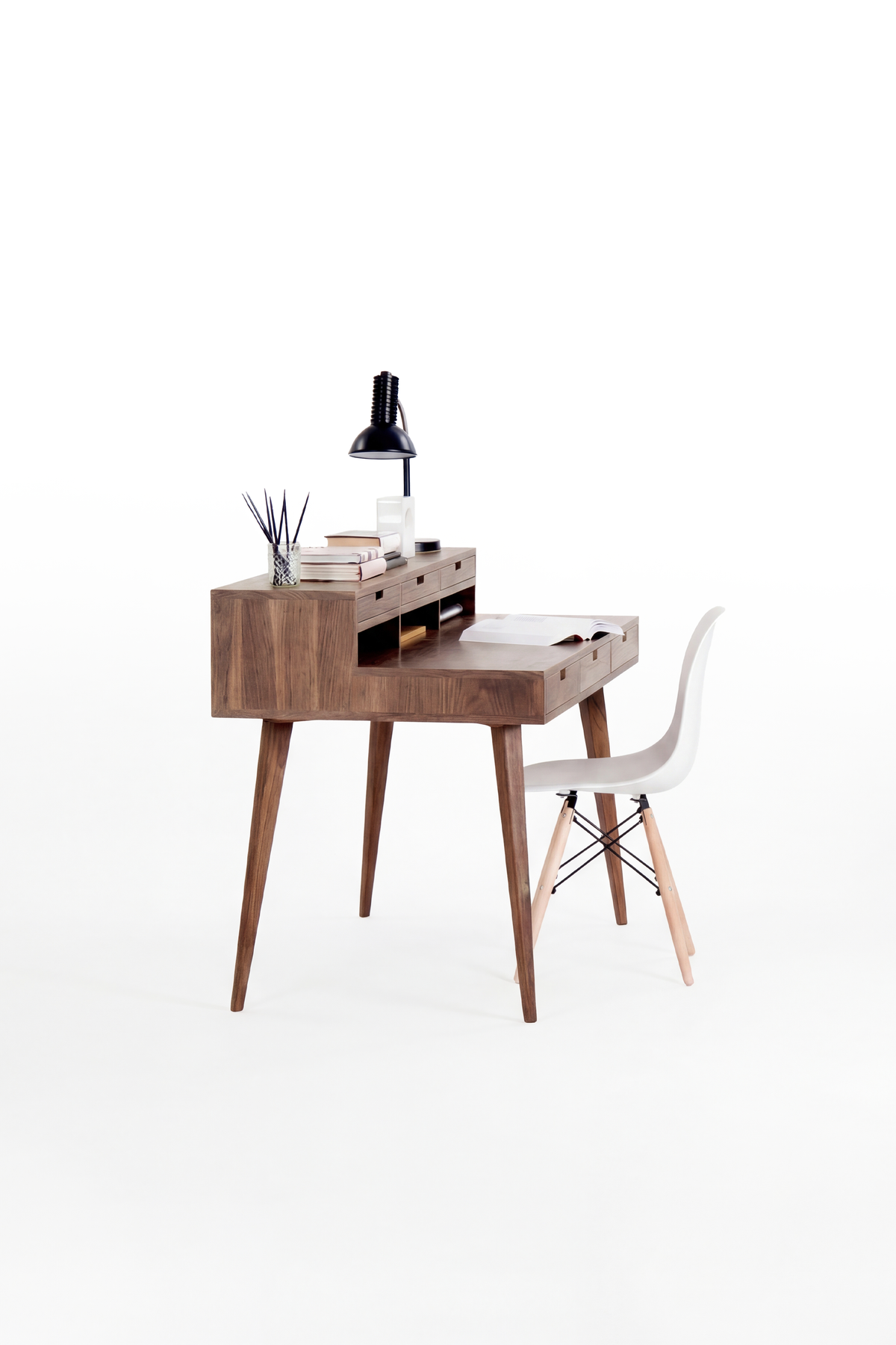 HEIM 140 desk in solid walnut seen from one end, with a white shell chair and a lamp on the hutch