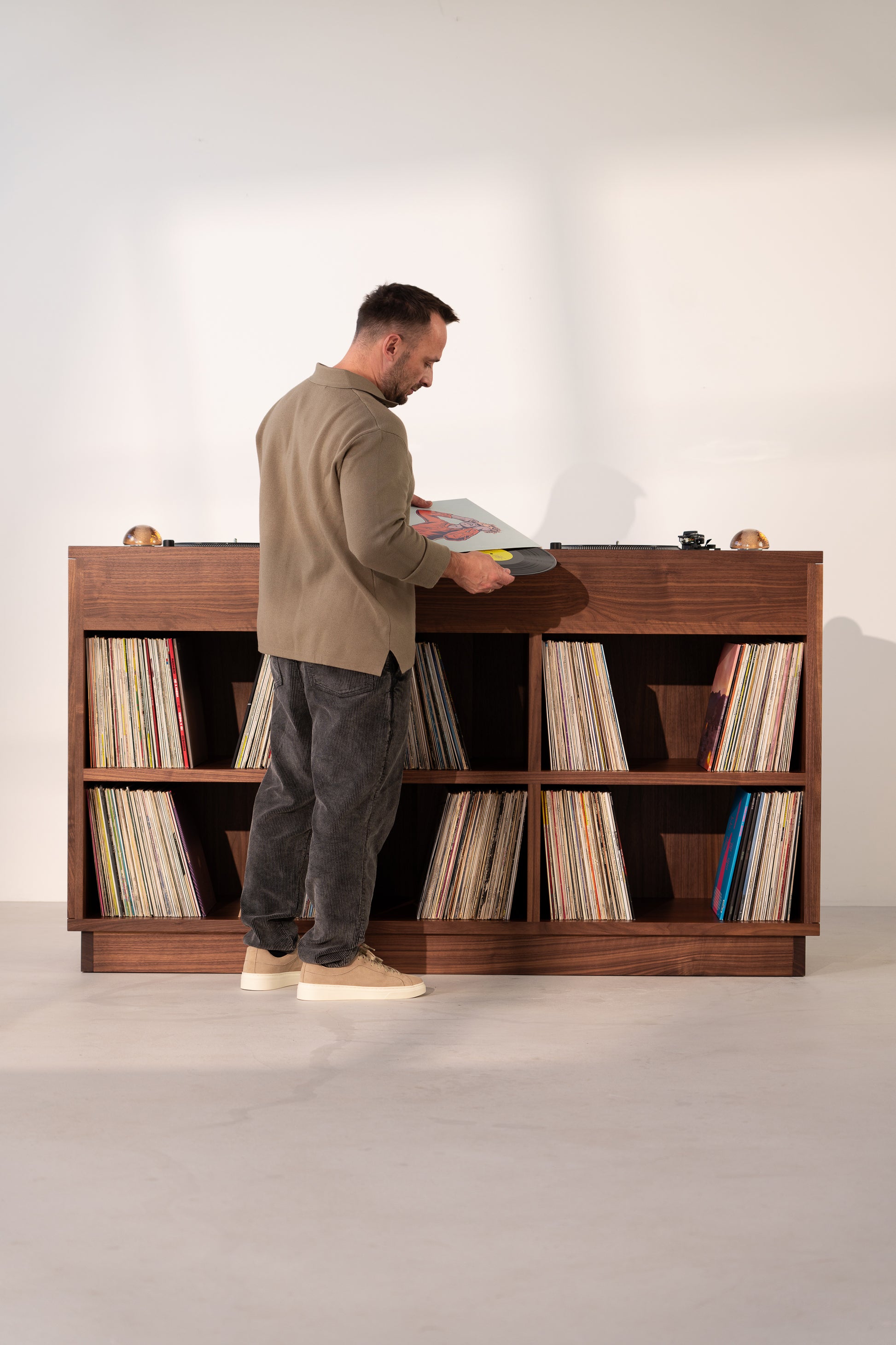 Man browsing vinyl records in a wooden shelf, facing a turntable.