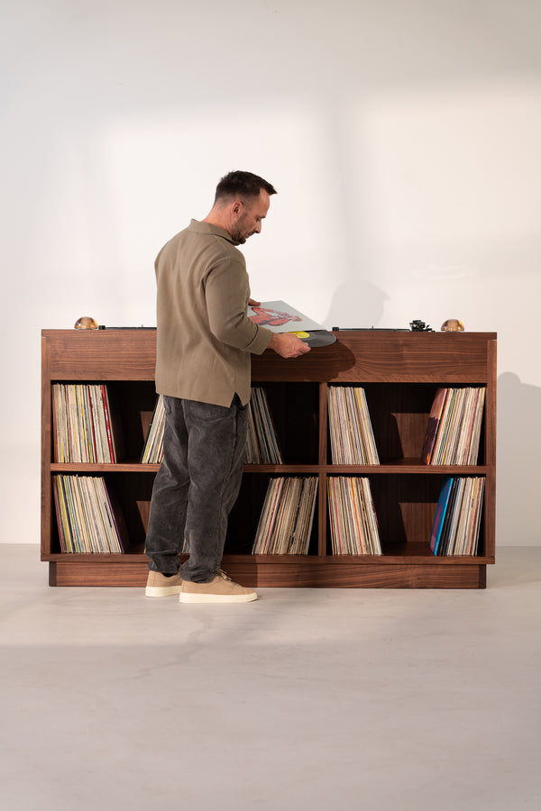 Man browsing vinyl records in a wooden shelf, facing a turntable.