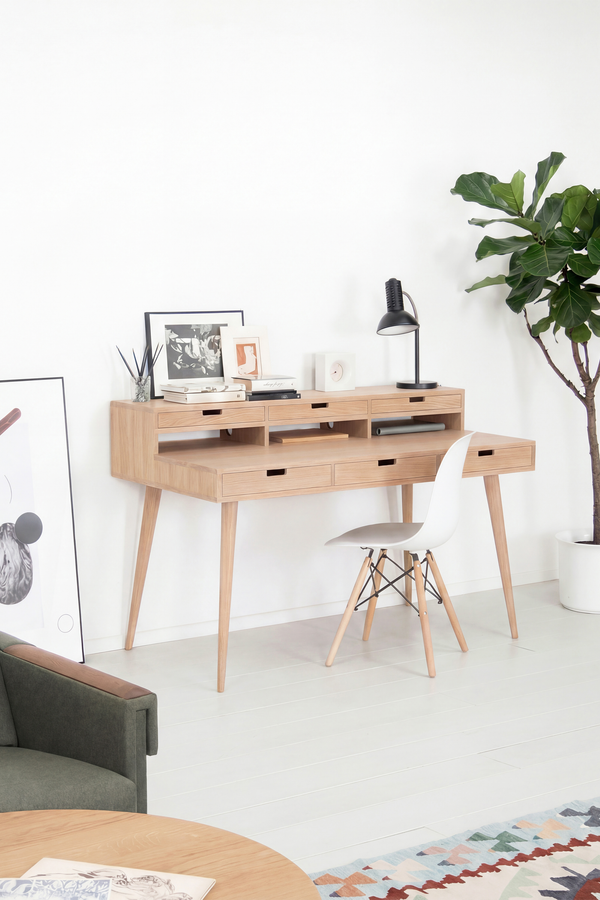 HEIM 140 desk with hutch in solid oak, angled in a living room with a white shell chair, black lamp and books