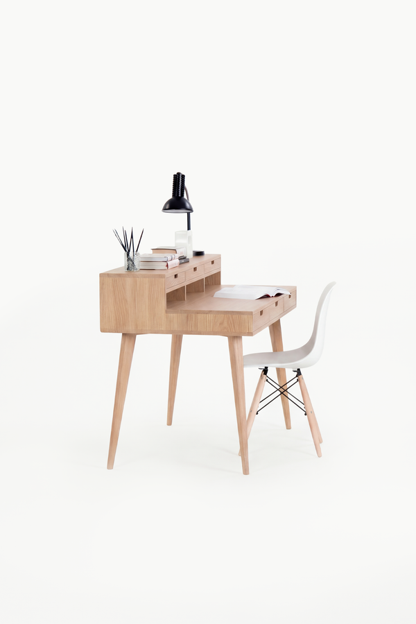 HEIM 140 desk in solid oak, seen from the short end with a white shell chair and books on the hutch