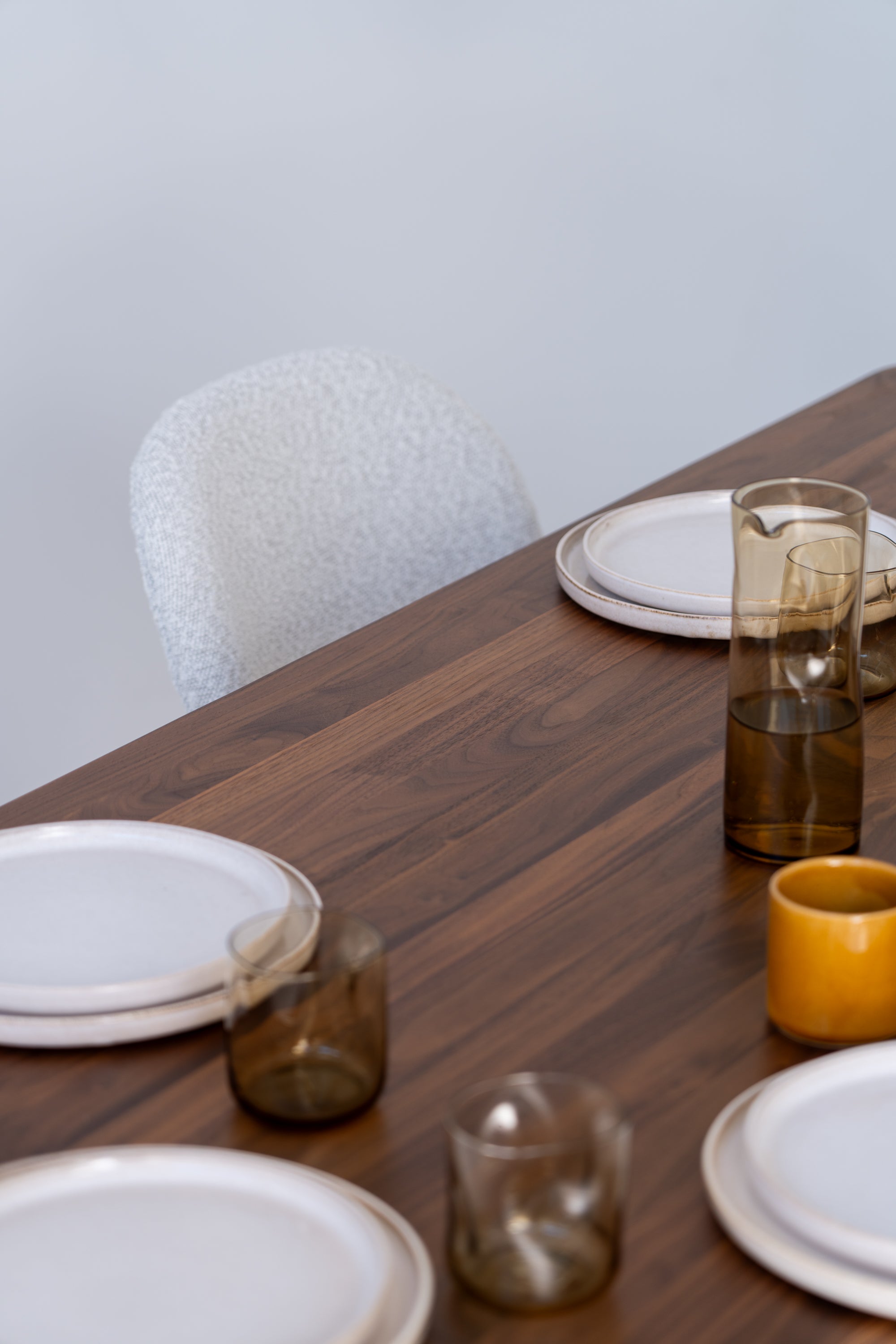 A wooden table set with white plates, brown glasses, and a yellow mug, with a white chair in the background.