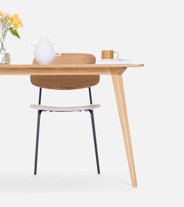 Wooden table and chair, with a vase of yellow flowers, a white teapot, and a yellow mug placed on the table.