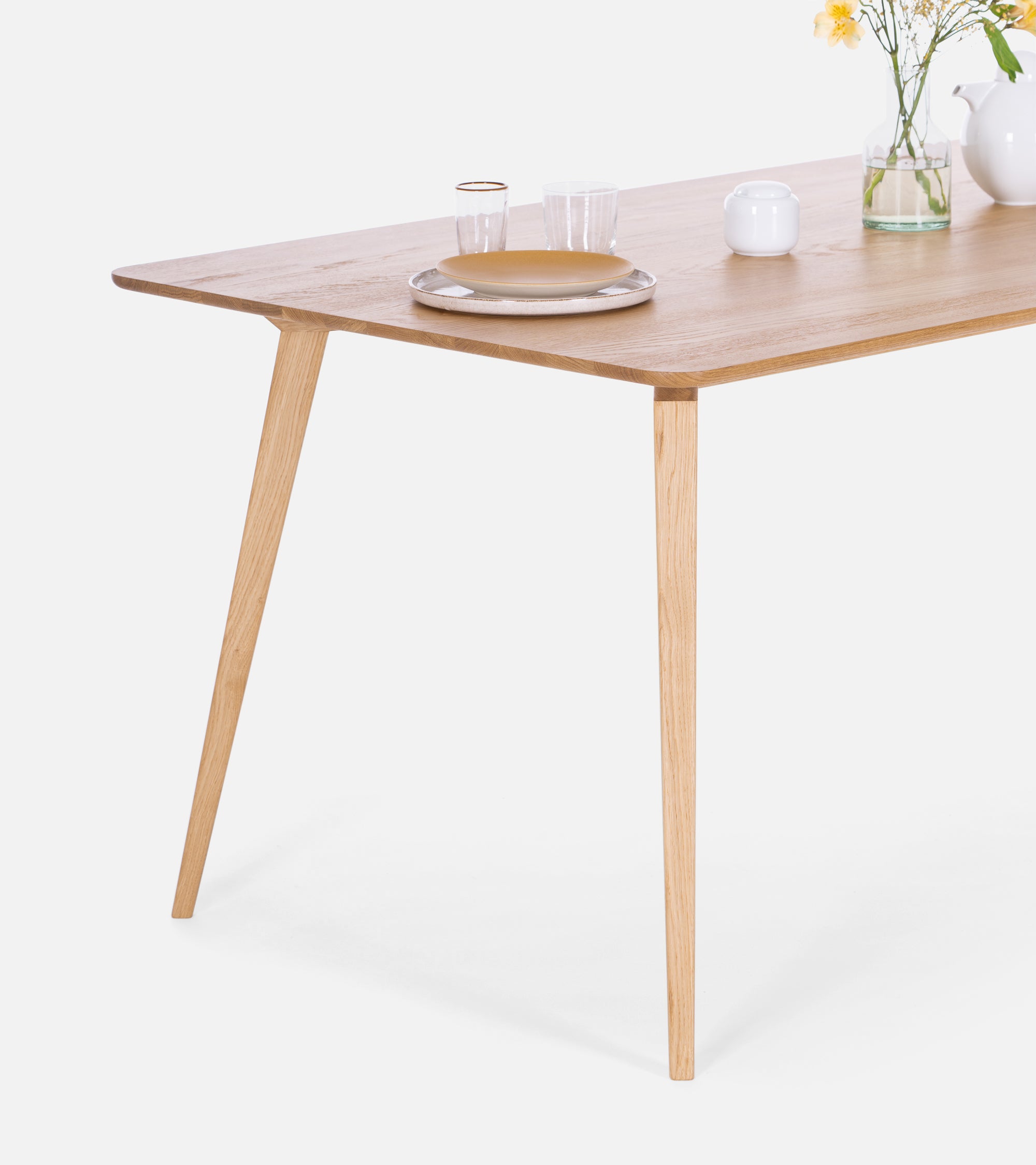 Simple wooden table set with glassware, dishes, and a vase of flowers.