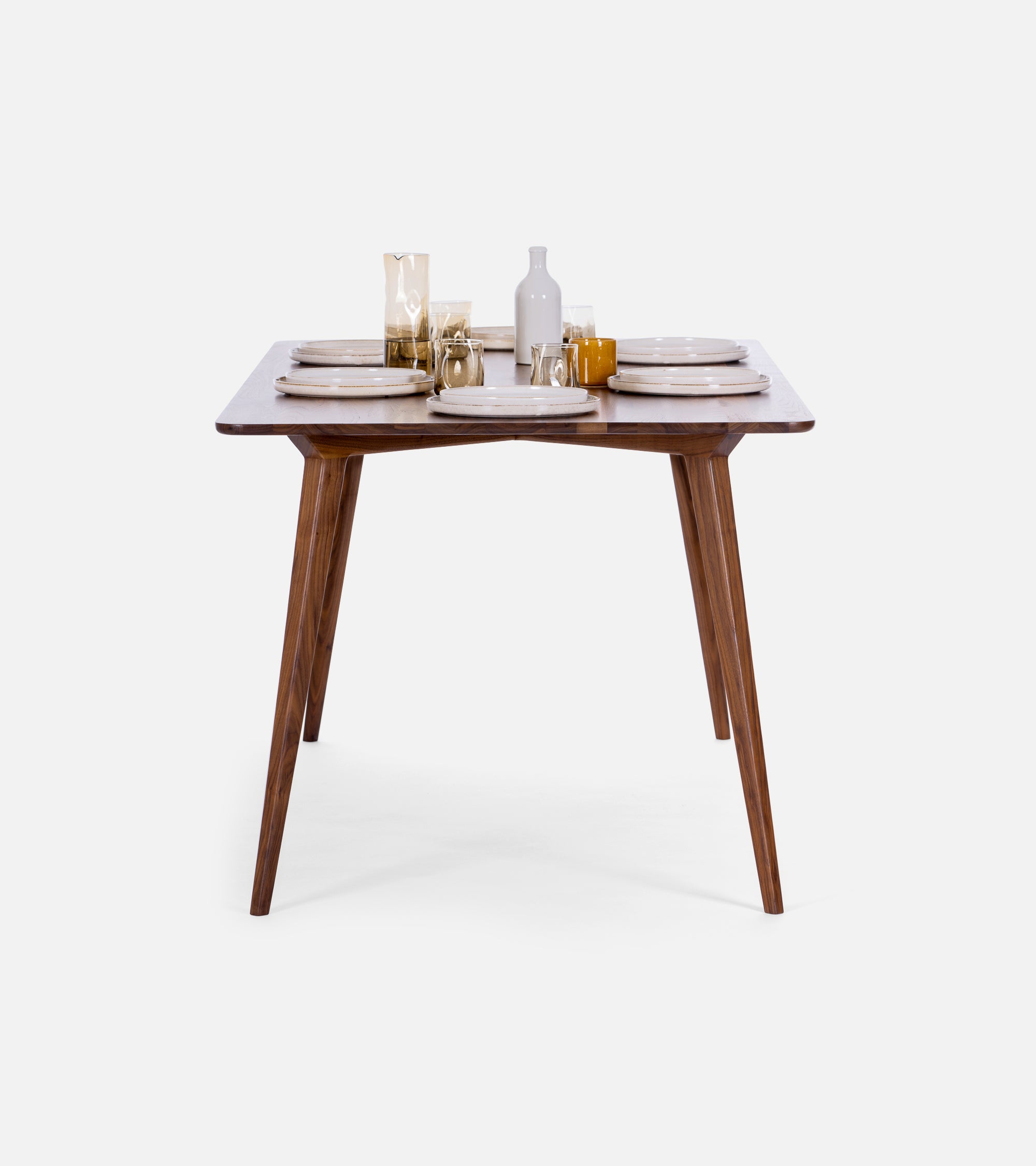 A set dining table with wooden legs, white plates, glasses, and a bottle against a plain background.