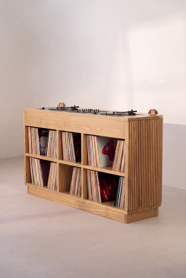 Angled rear view of LOOP in solid oak, with six compartments filled with records, a grooved side and turntables on top