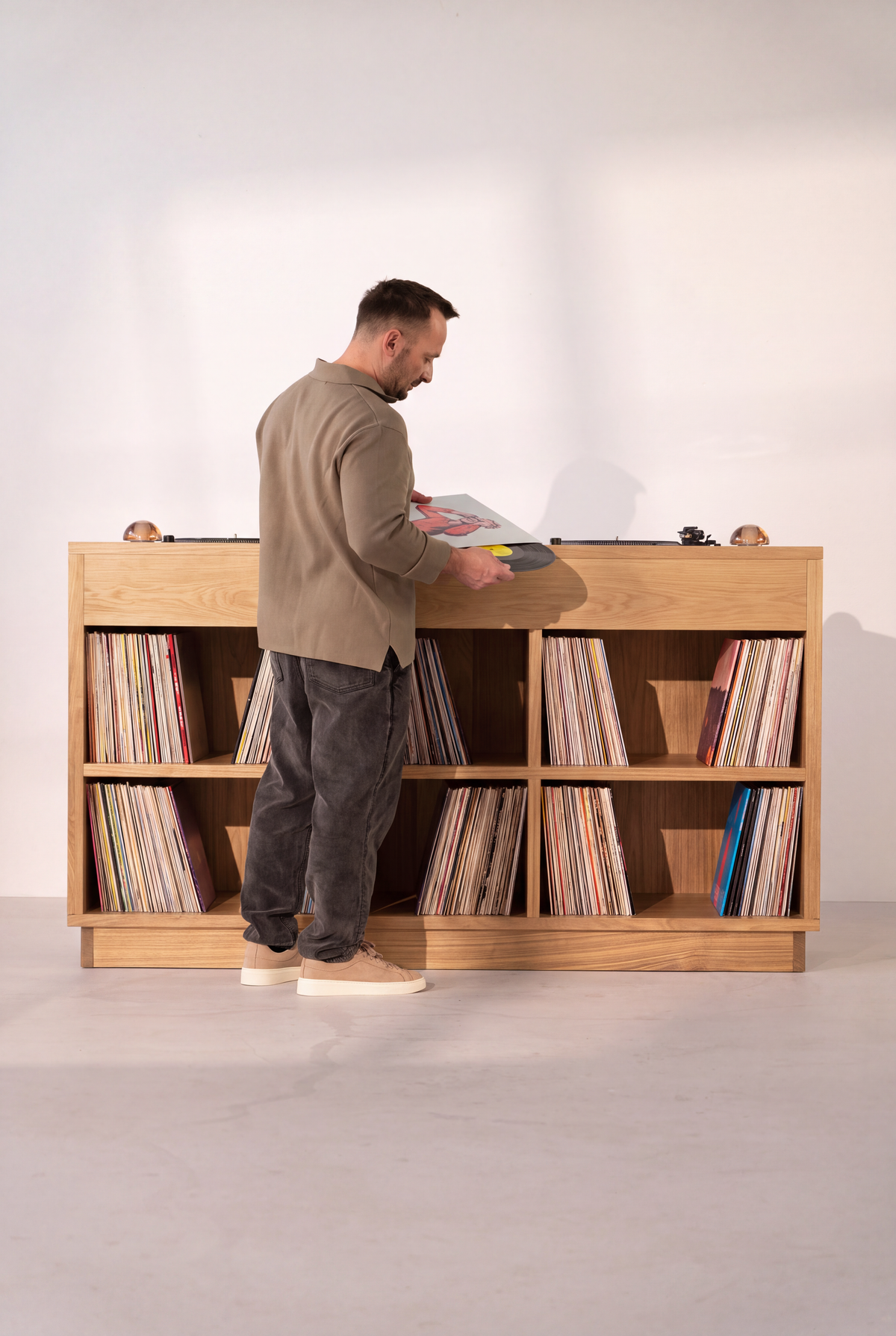 Rear view of LOOP in solid oak, with six open compartments full of records and a man handling a record