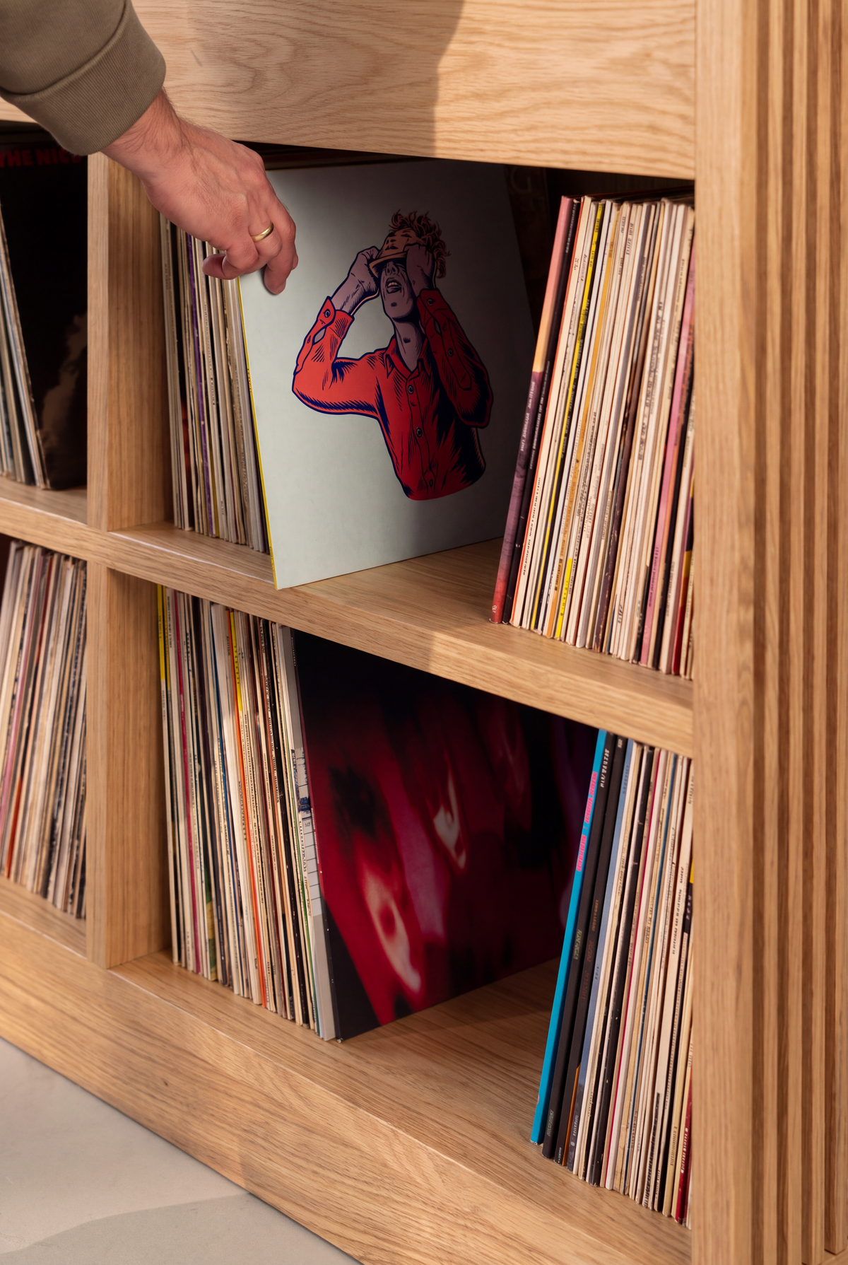 Close-up of a hand pulling a record from a filled rear compartment of LOOP in solid oak