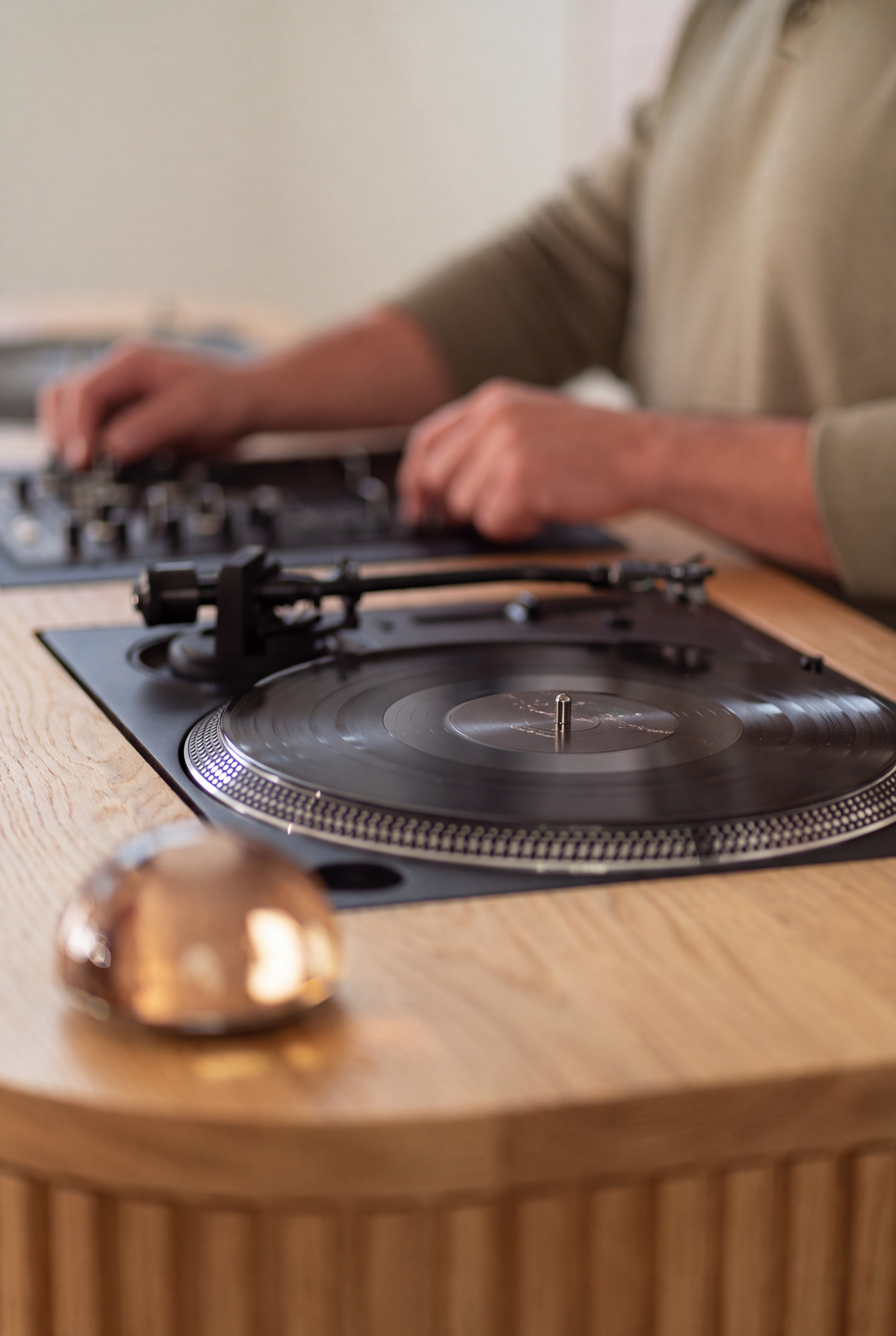 Close-up of LOOP in solid oak with a flush-mounted turntable, hands on the mixer and a glass dome light