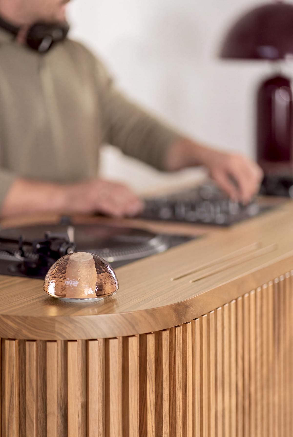 Glass dome light on the rounded top edge of LOOP in solid oak, with a DJ blurred at the mixer behind