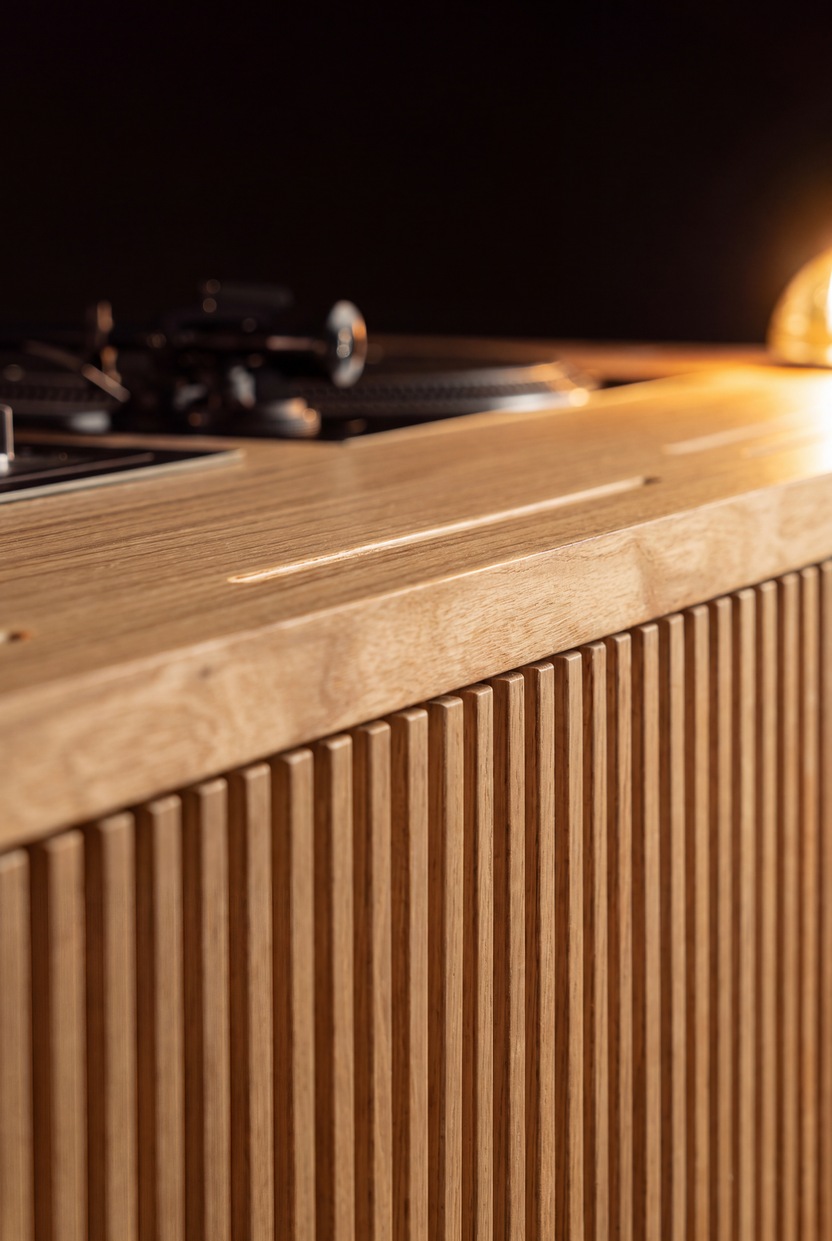 Close-up along the top edge of LOOP in solid oak, showing a narrow slot, a turntable and a lit glass dome light