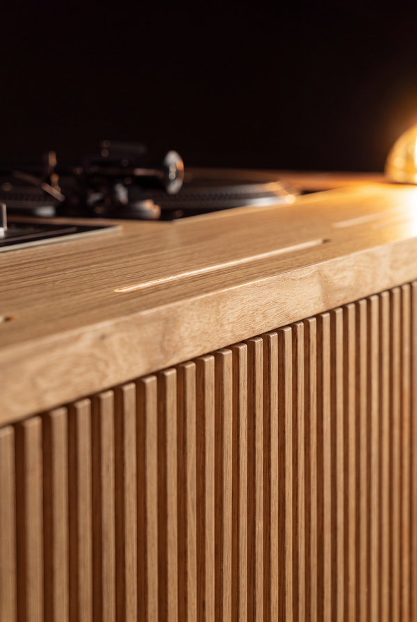 Close-up along the top edge of LOOP in solid oak, showing a narrow slot, a turntable and a lit glass dome light