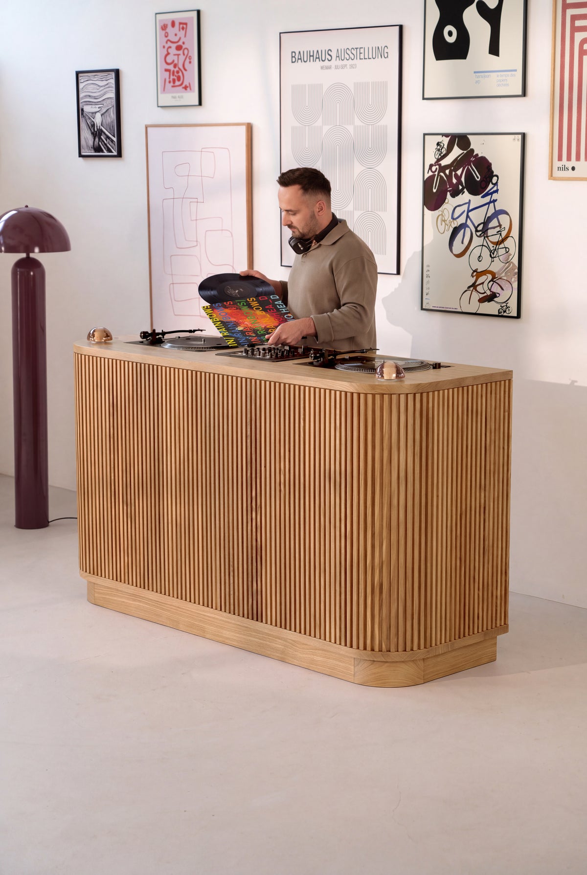 A DJ wearing headphones holds a record behind the LOOP DJ station in solid oak, seen at an angle