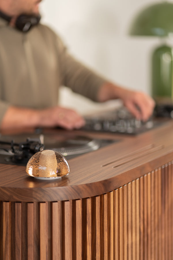 A person using DJ equipment on a wooden table, with a small glass dome in focus.