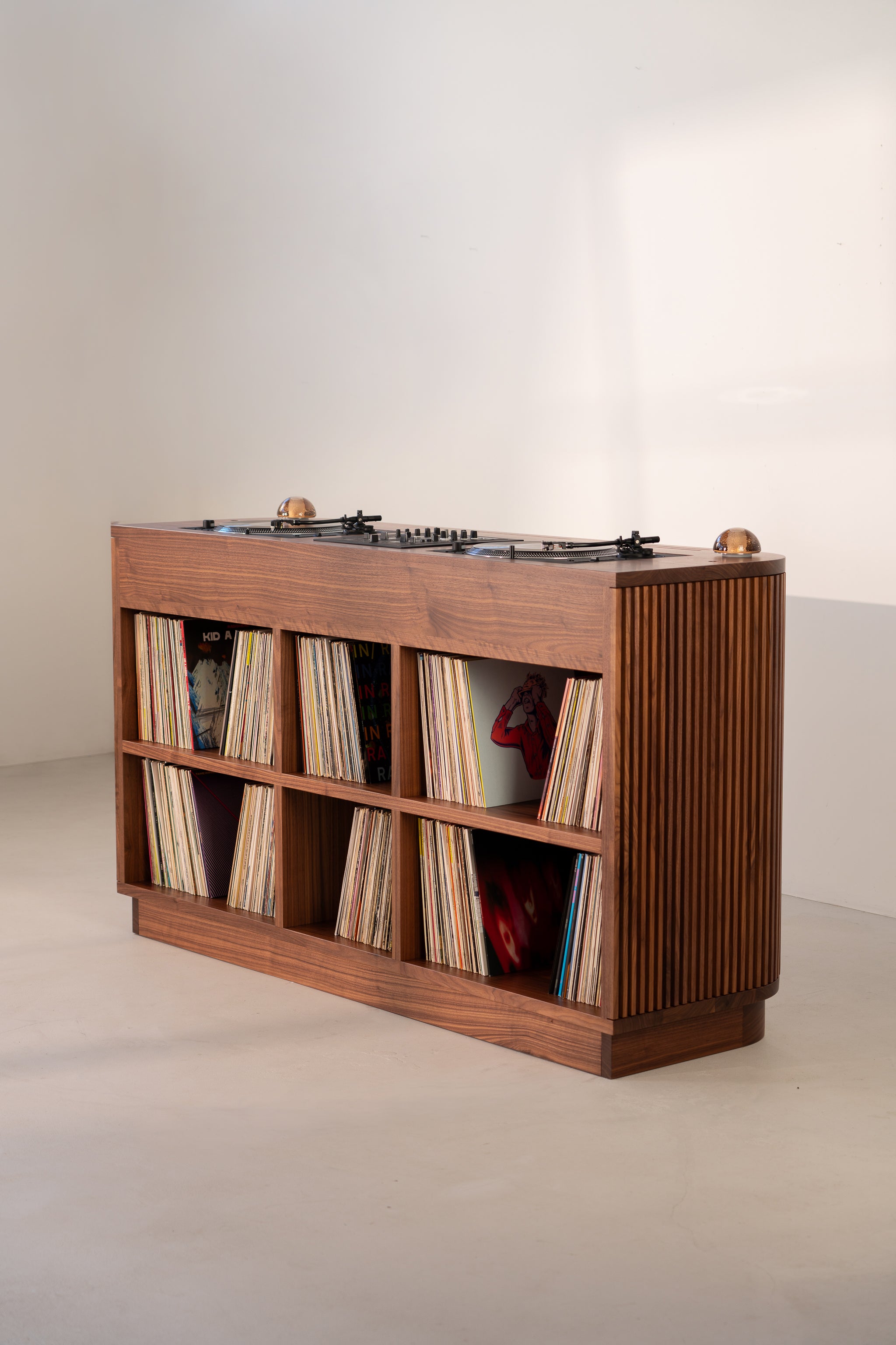 Wooden cabinet with vinyl records and turntables on top, set against a white wall.