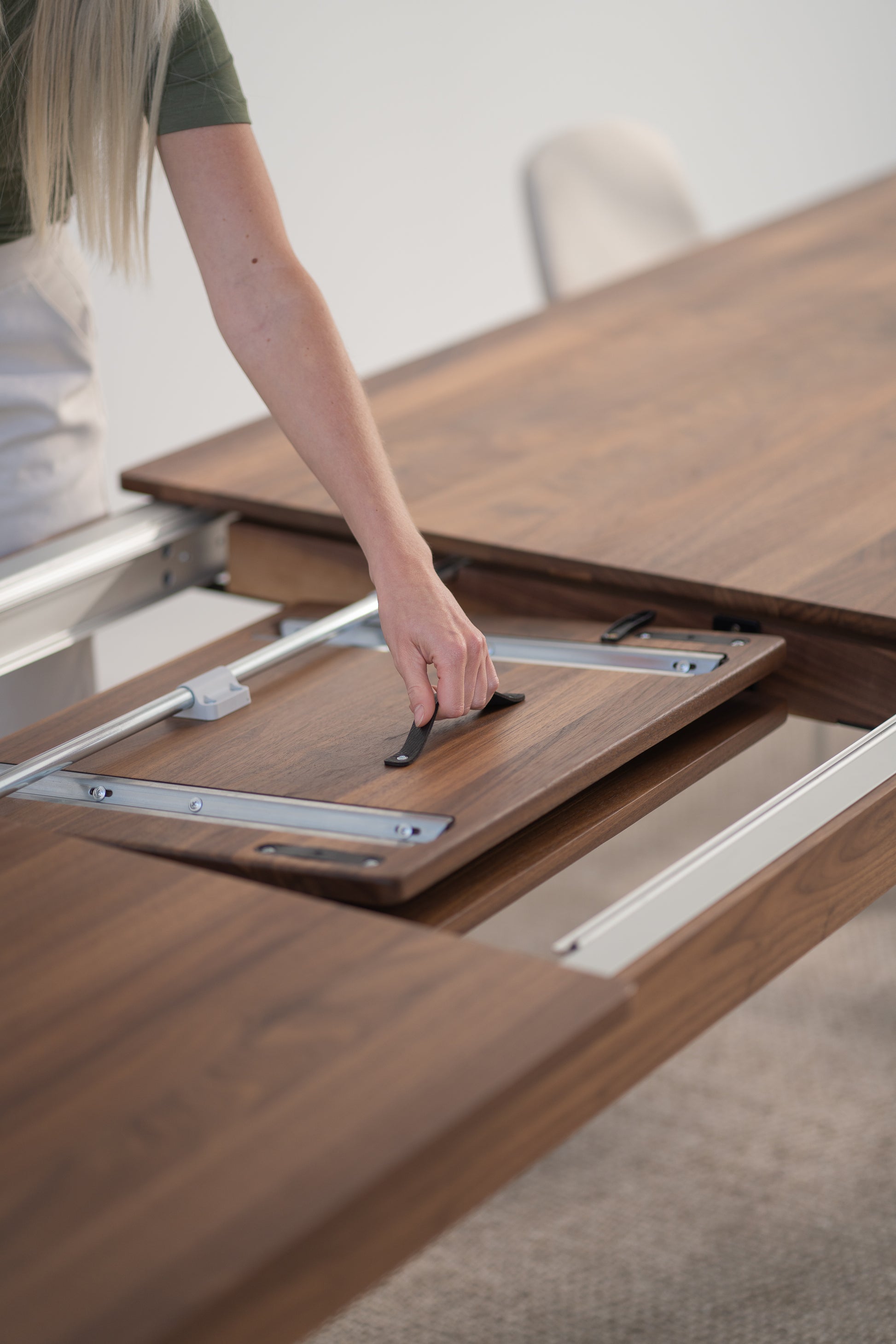 Person's hand extending a wooden dining table by sliding a hidden leaf into place.