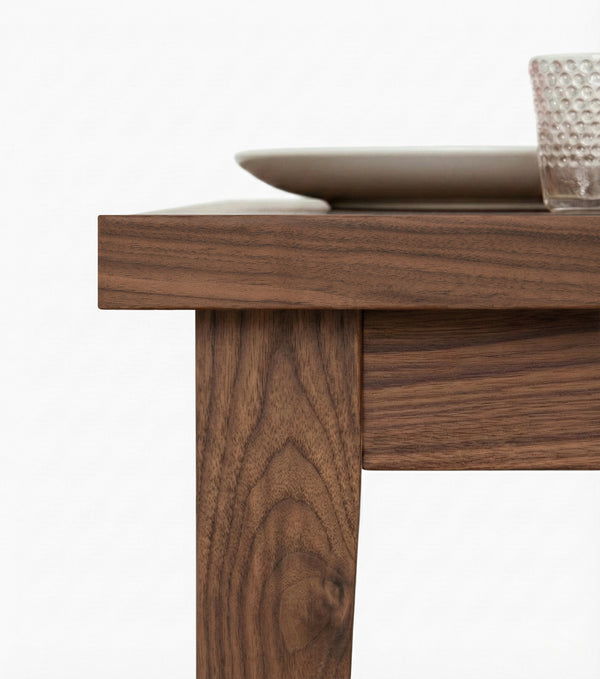 Close-up of a solid walnut table corner highlighting the natural wood grain and seamless leg-to-top joinery.