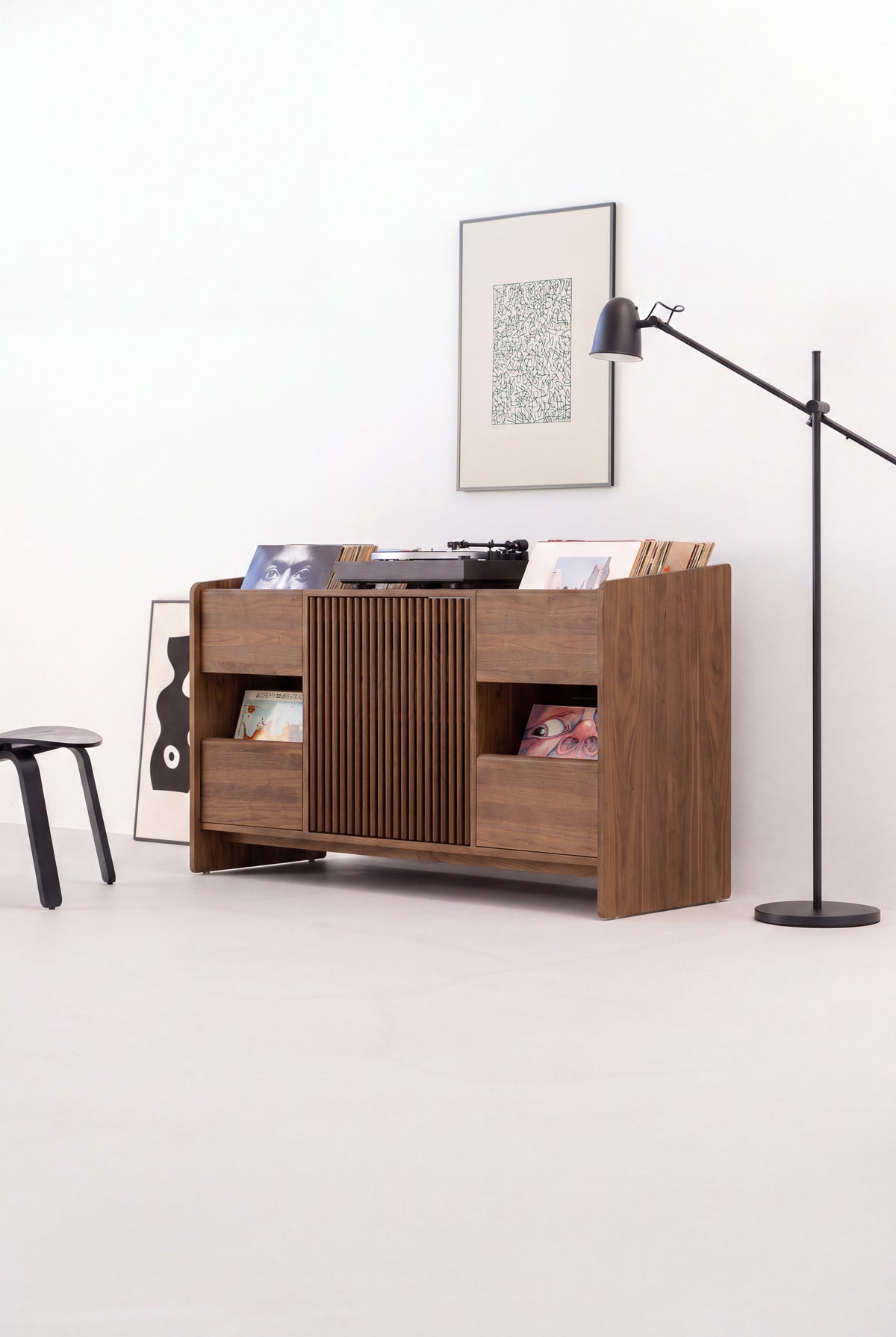 FUSE X in solid walnut seen at an angle in a light room, with a black stool and floor lamp beside it