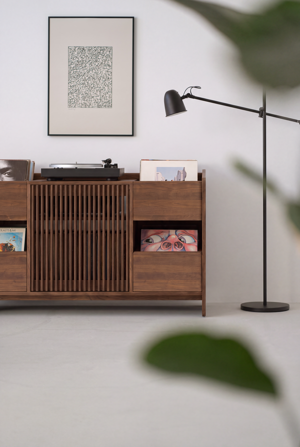 Front view of the FUSE X in solid walnut, partly framed by a blurred plant leaf, with a turntable and records on top