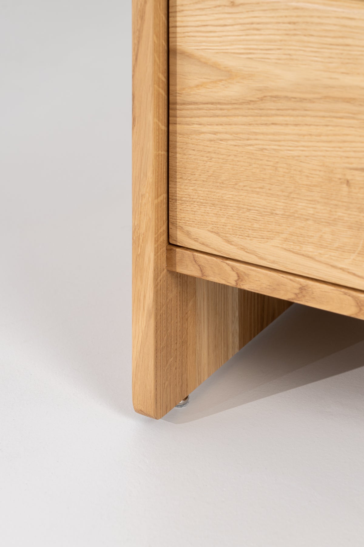 FUSE XX in solid oak, close-up near floor level of the side panel and metal foot beneath the drawer front
