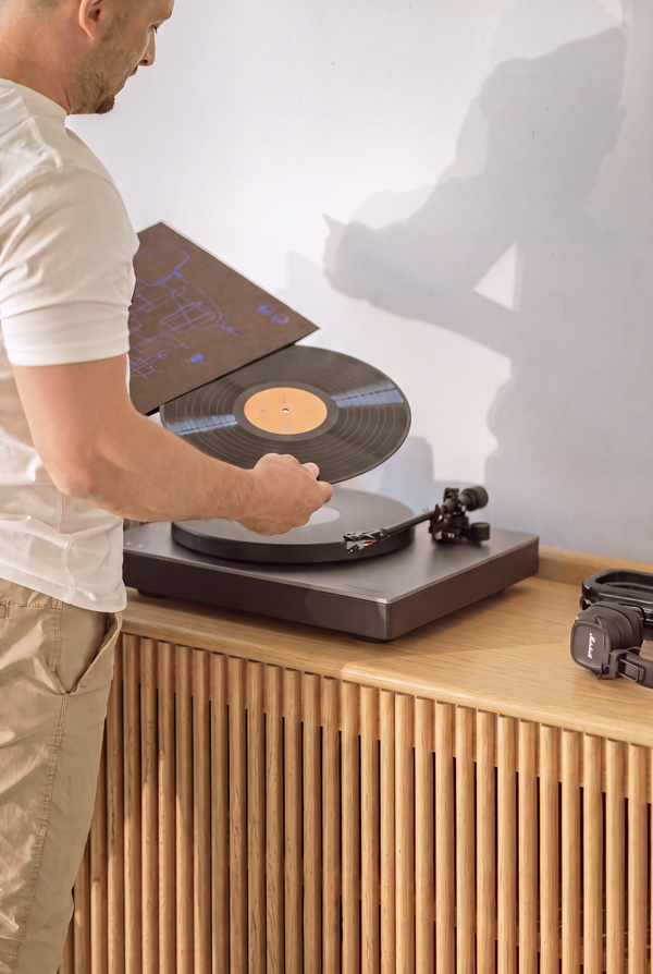 A man places a record on the turntable above the slatted door of the FUSE XX in solid oak