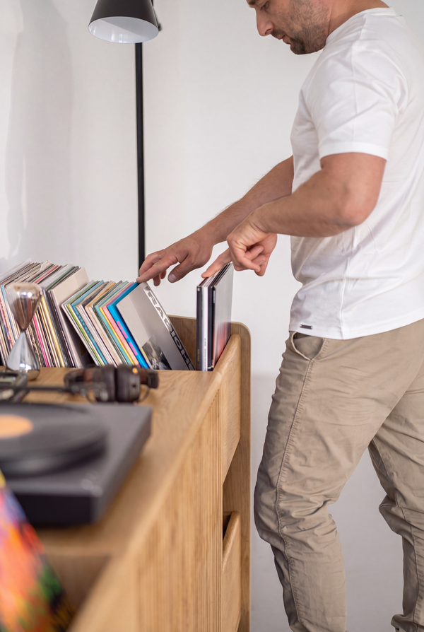 A man browses records in the end niche of the FUSE XX in solid oak, with the turntable in the foreground