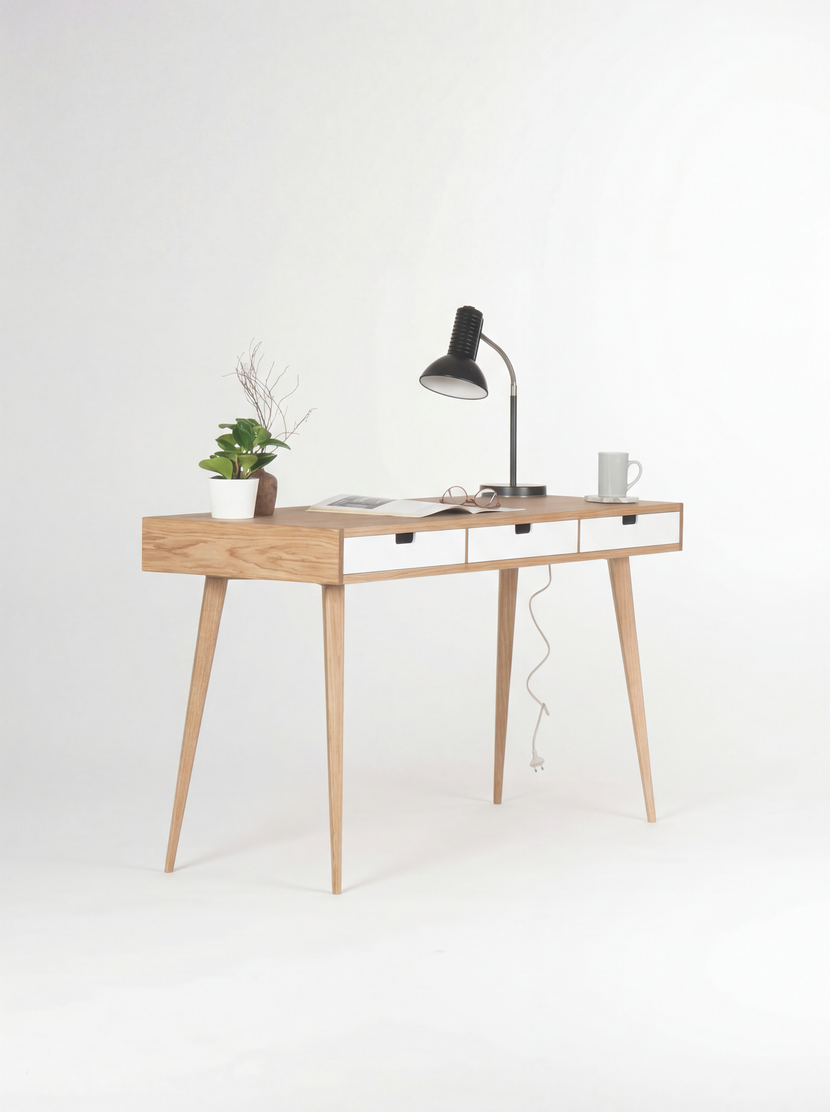HEIM 140 desk in oak wood, angled view with white fronts, an open magazine and a lamp cable hanging behind