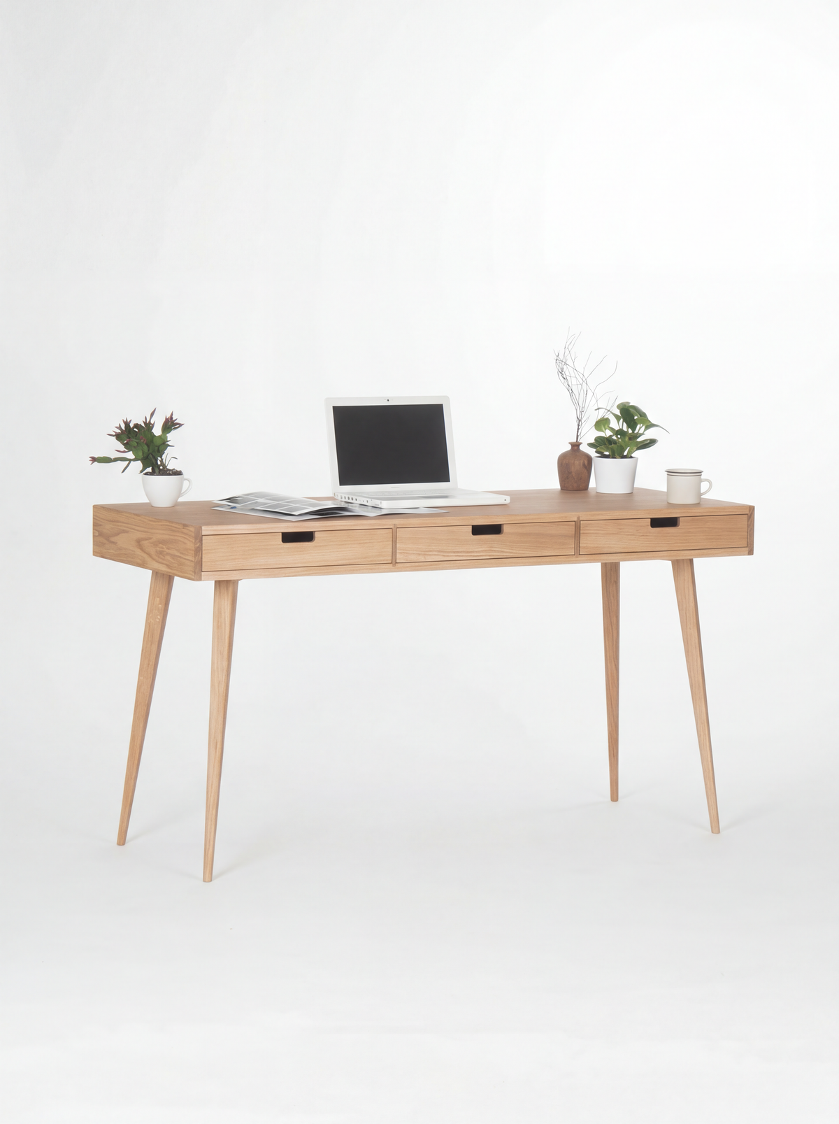 HEIM 140 home office desk in oak wood, angled view with three wooden drawer fronts, a laptop and two plants