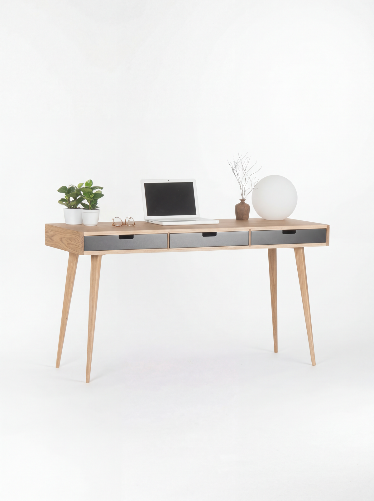 HEIM 140 desk in oak wood, full view with black fronts, splayed legs, laptop, plants and globe lamp