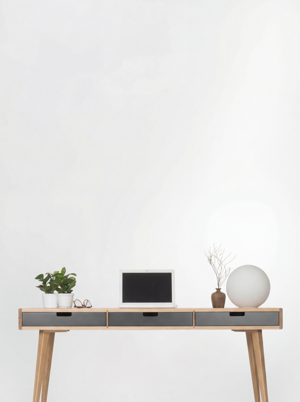 HEIM 140 desk in oak wood against a white wall, with black drawer fronts, a laptop, plants and a globe lamp
