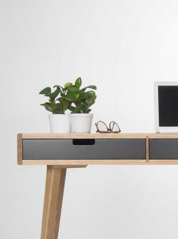 HEIM 140 desk in oak wood, close-up of a black drawer front and cut-out grip below plants and glasses