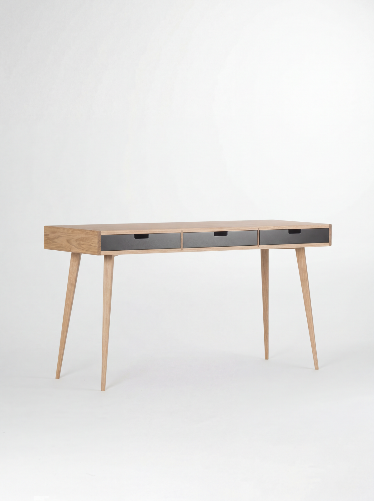 HEIM 140 desk in oak wood, shown empty at a three-quarter angle with three black drawer fronts on a white background