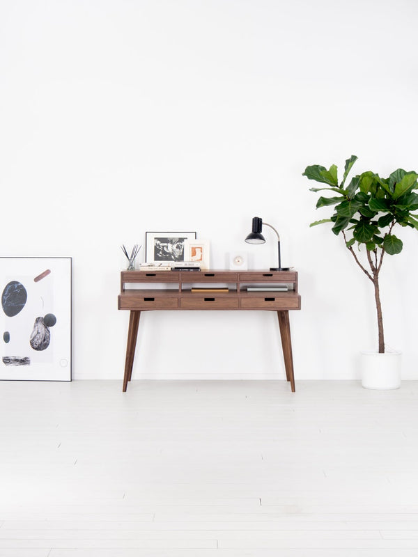 Mid-century modern console with decor, lamp, and plant in white room.