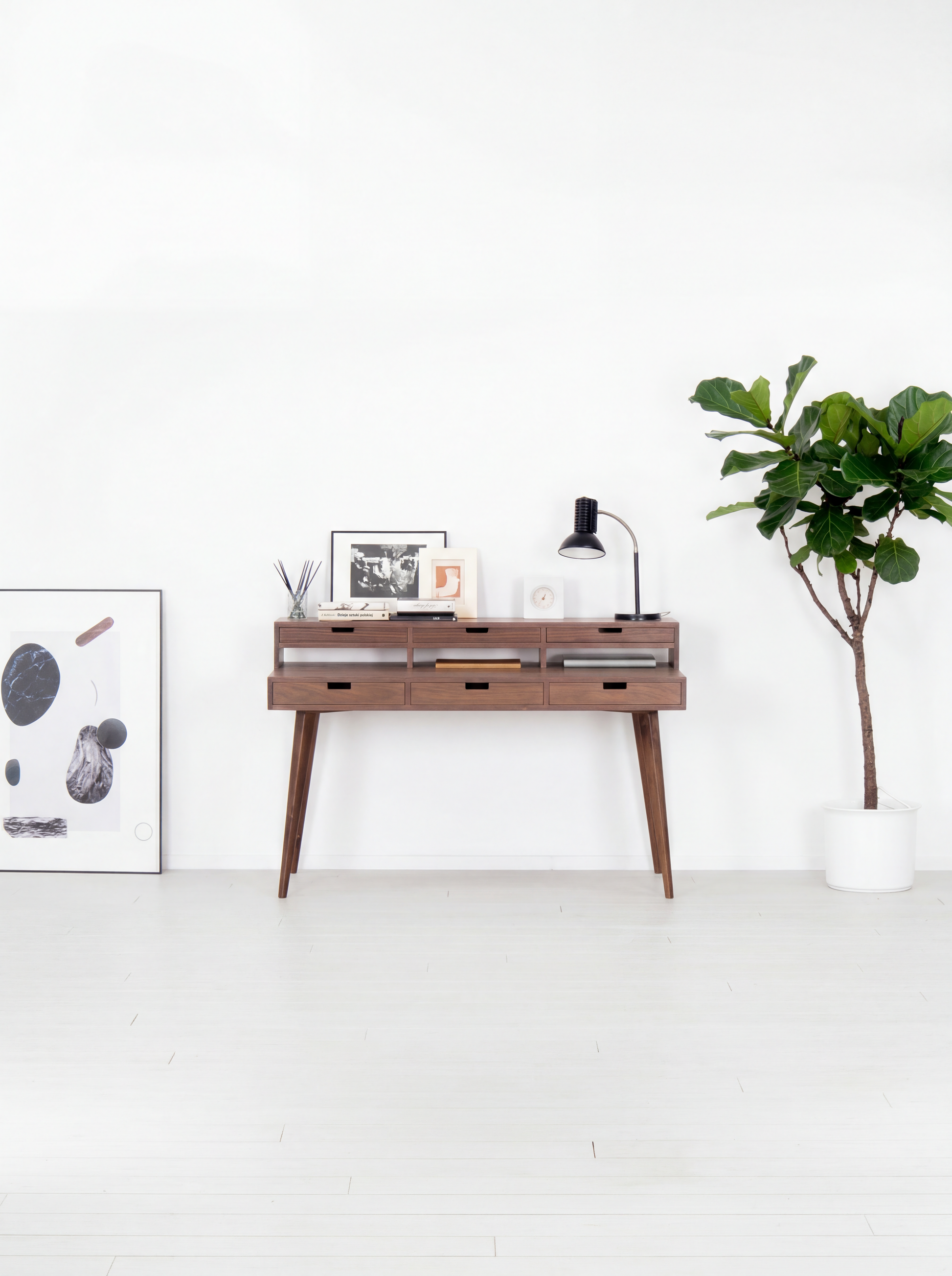 Mid-century modern console with decor, lamp, and plant in white room.