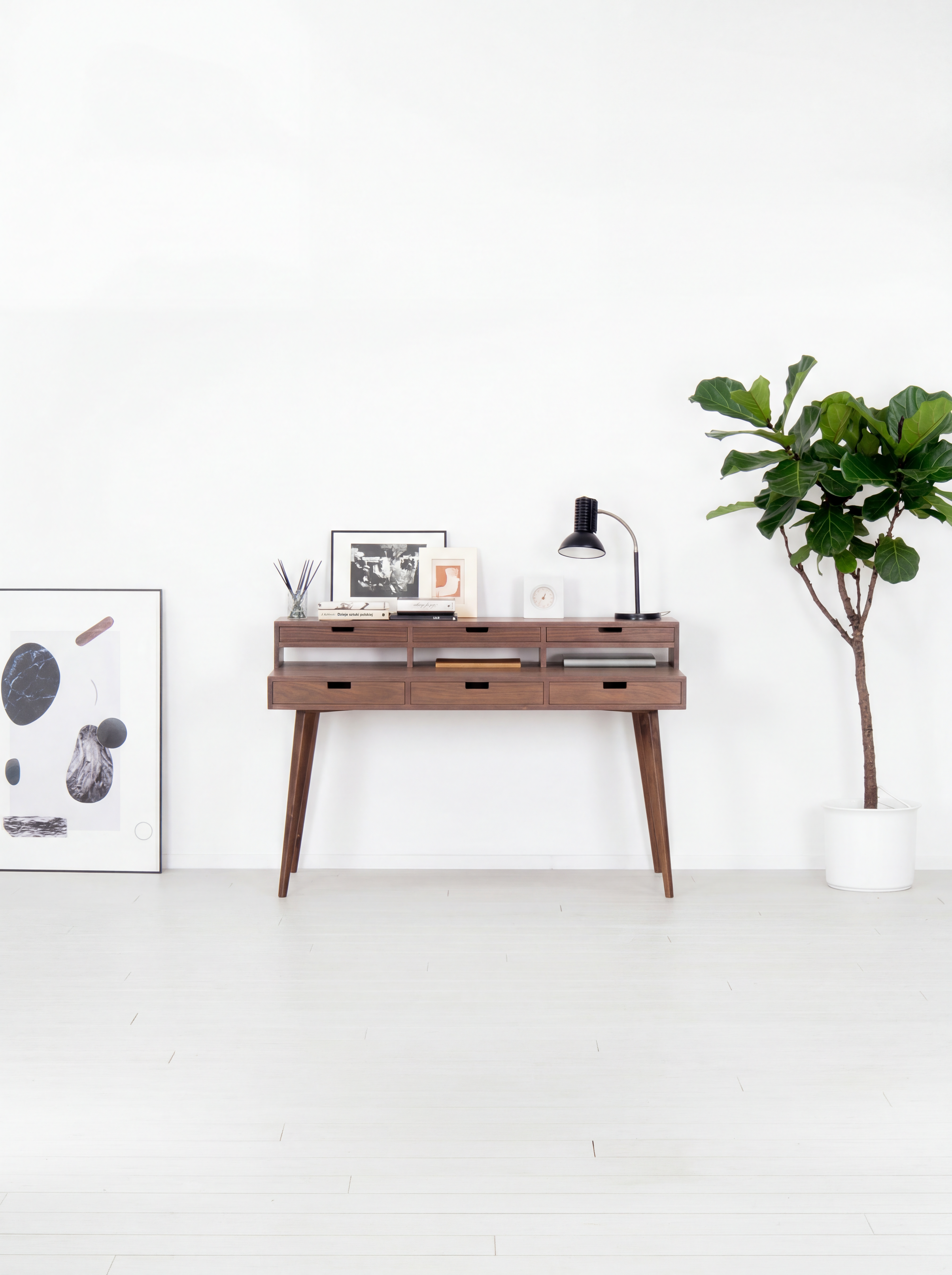 Mid-century modern console with decor, lamp, and plant in white room.