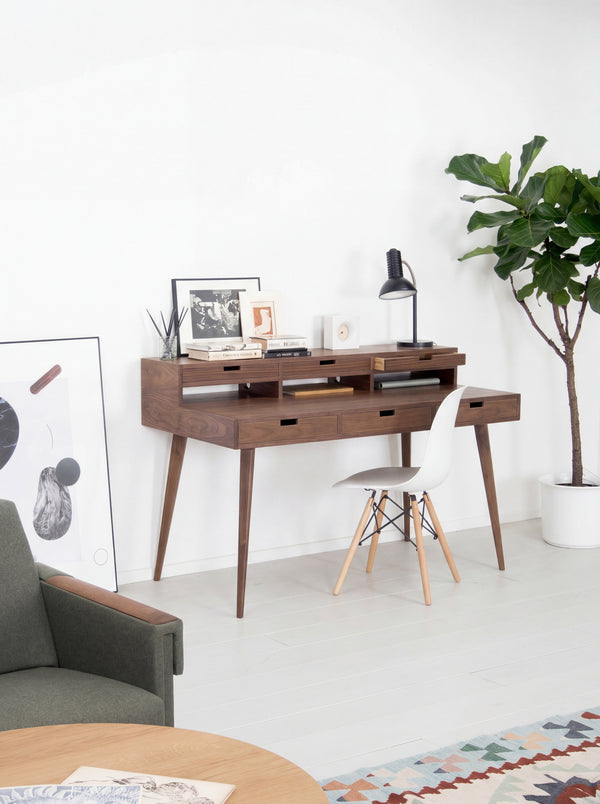 Mid-century modern office with a wooden desk, white chair, framed pictures, and a potted plant.