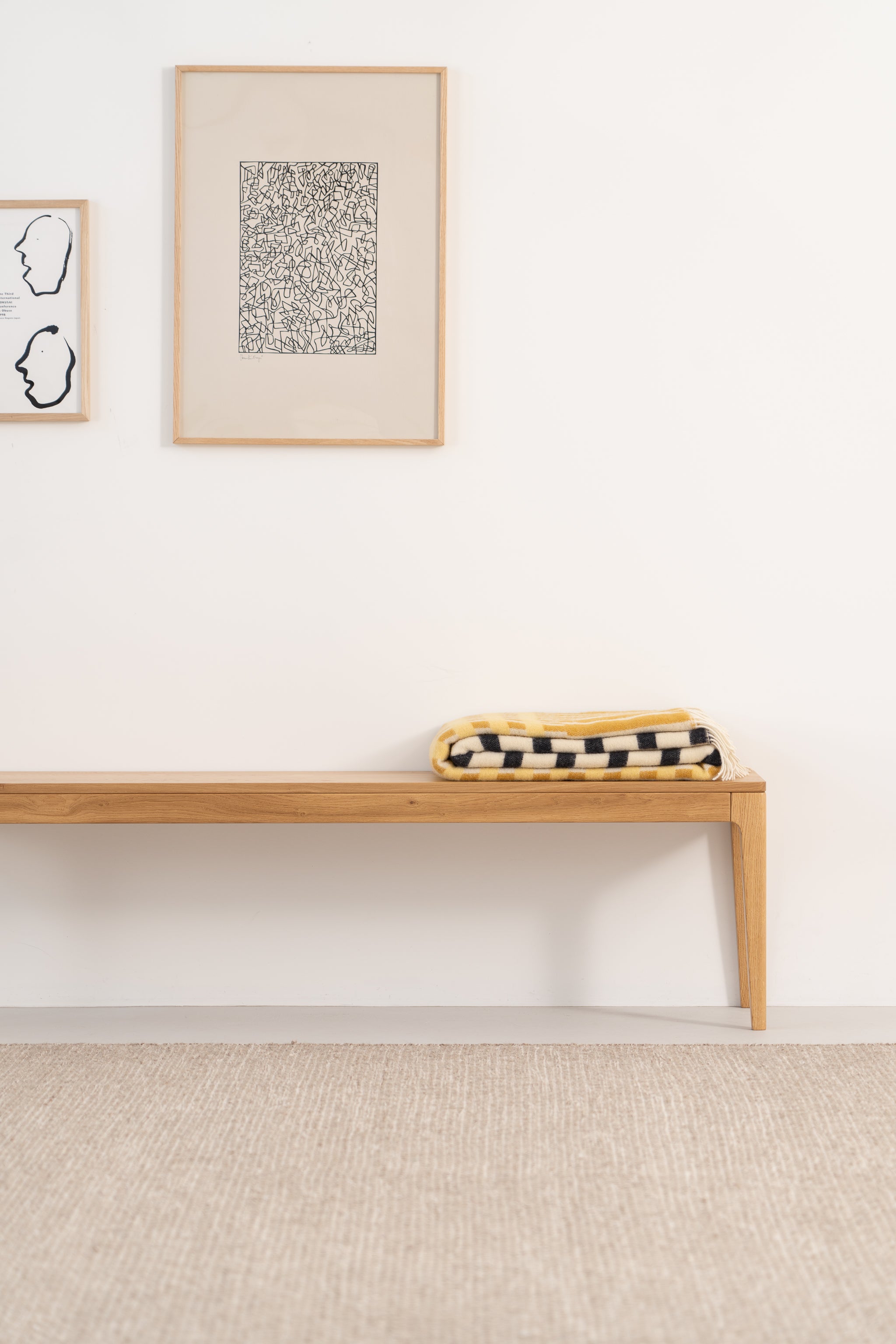 Minimalist bench with a checked blanket and framed abstract art on the wall.